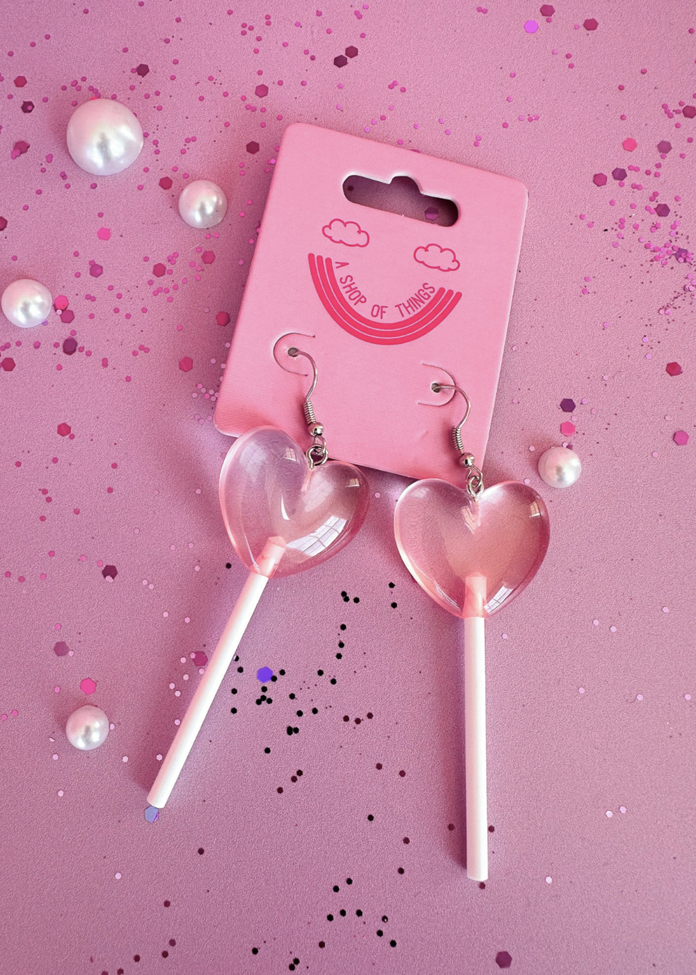 Heart-shaped lollipop earrings on a pink background with a pink card.