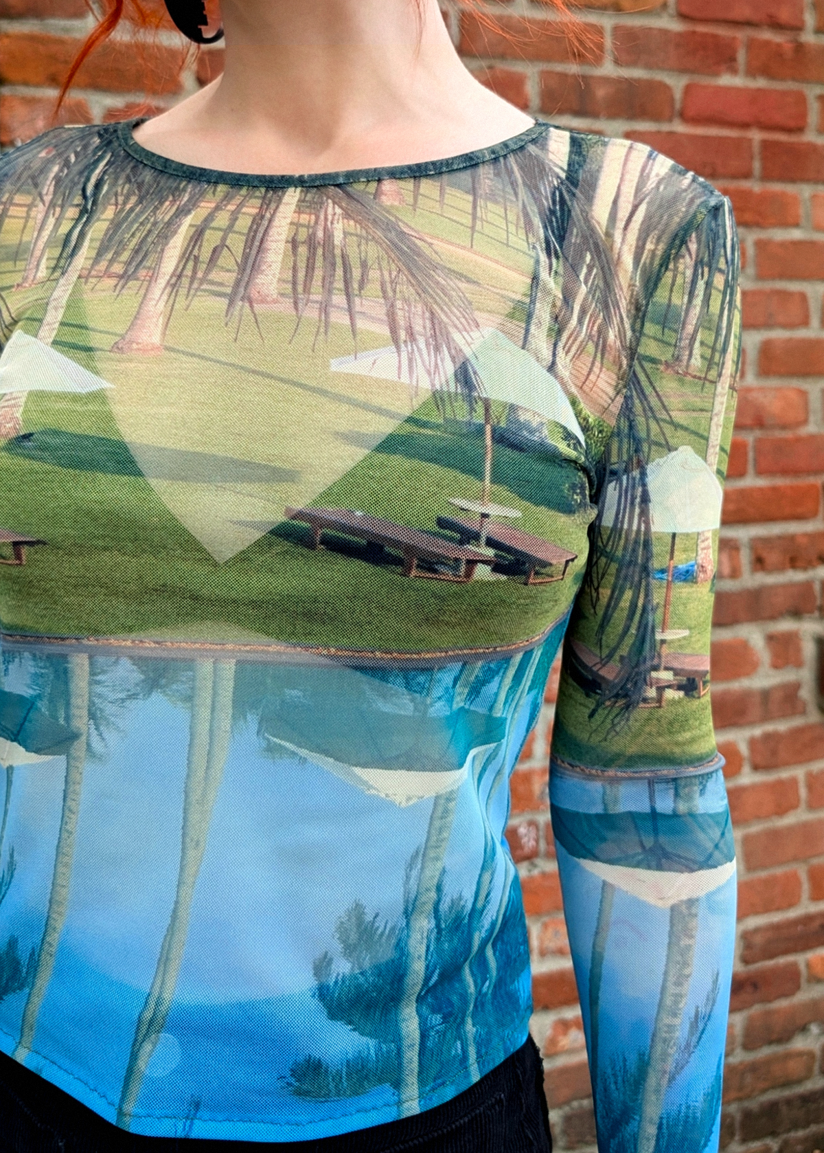 Long-sleeve shirt with a scenic print of a pool and palm trees against a brick wall.