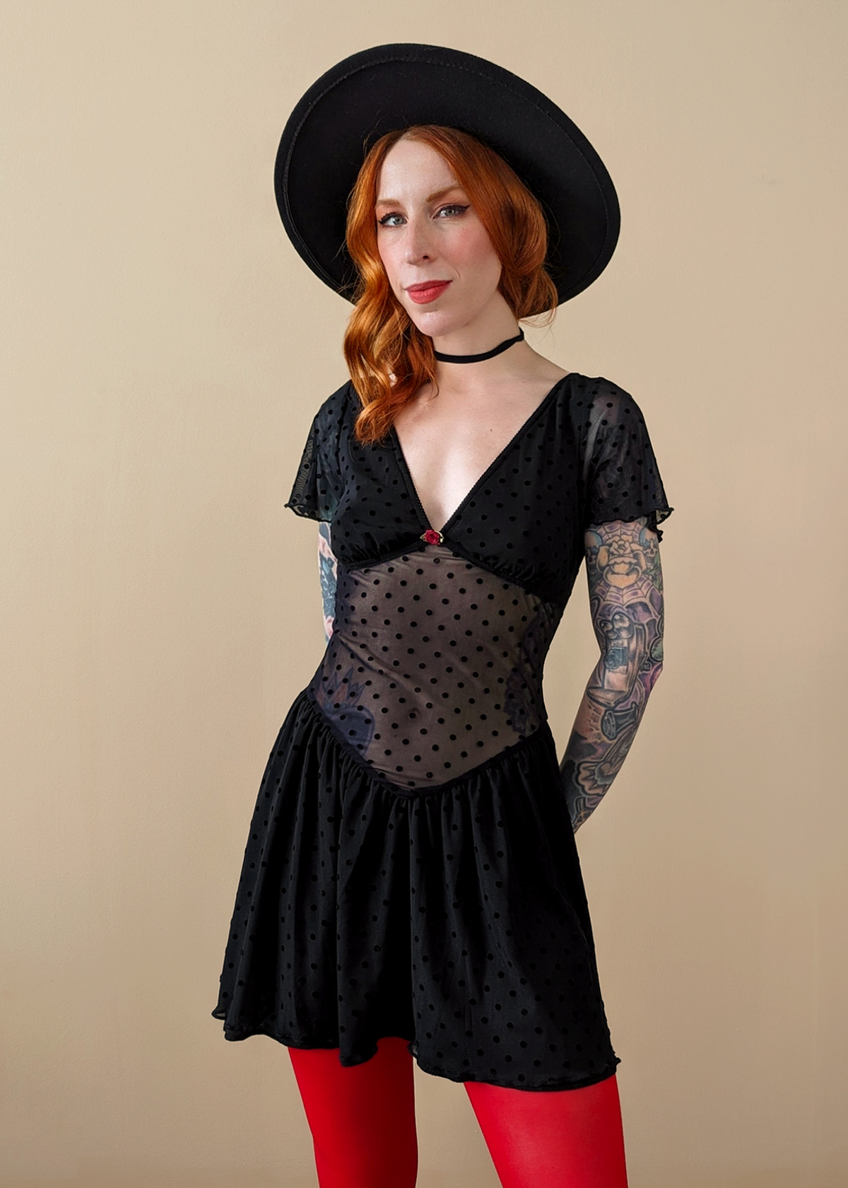 90s inspired black mesh mini dress with black velvet flocked dots allover. Features flutter short sleeves, v-neckline with red satin rosette, sheer waist, and floaty skirt. By Motel Rocks