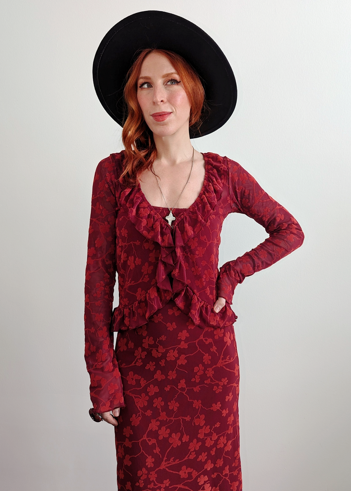 90s inspired burgundy red ruffled cardigan top made of a slinky mesh fabrication with flocked velvet floral design. Deep v-neckline, hook and eye closure at front. Long sleeves. By Motel Rocks