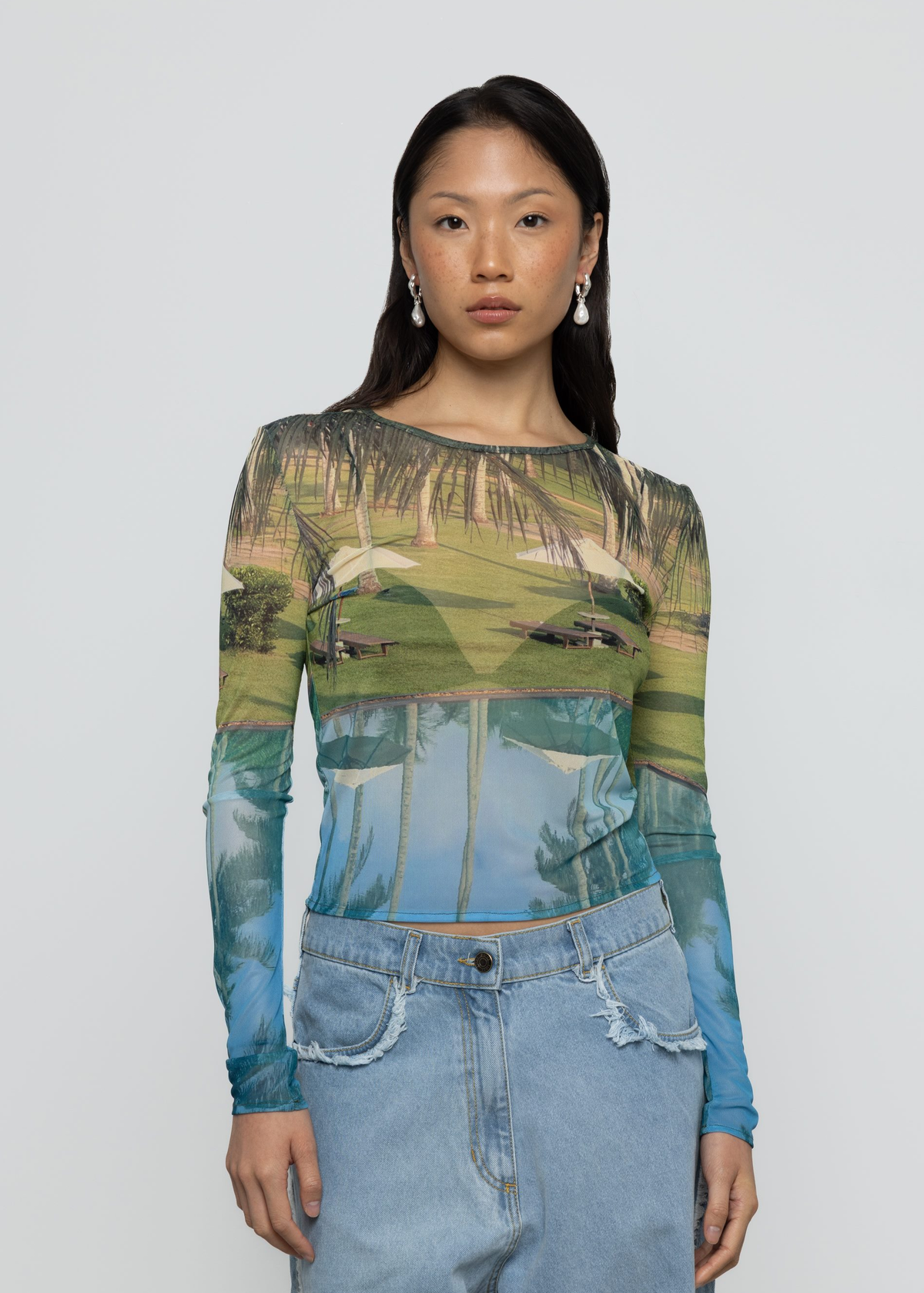 Woman wearing a long-sleeve top with tropical-themed print against a plain background