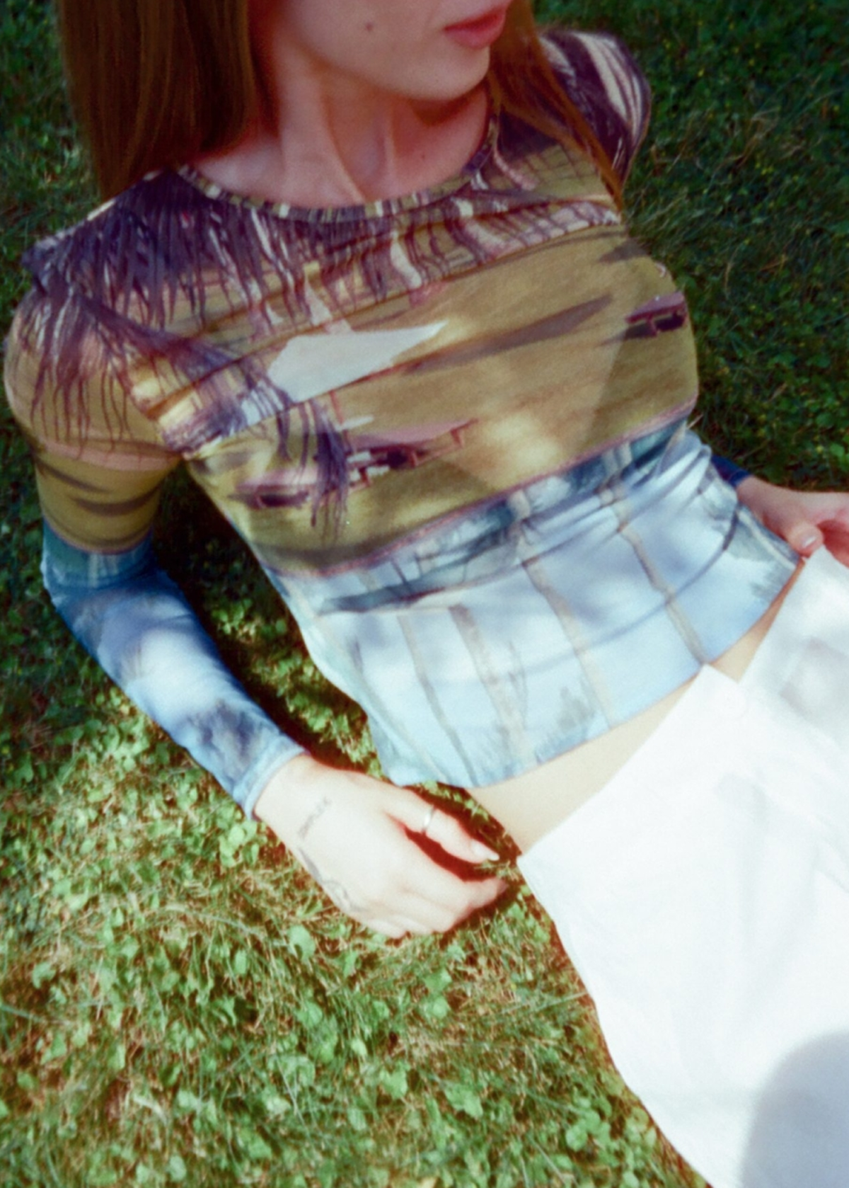 Person wearing a patterned mesh shirt and skirt sitting on grass