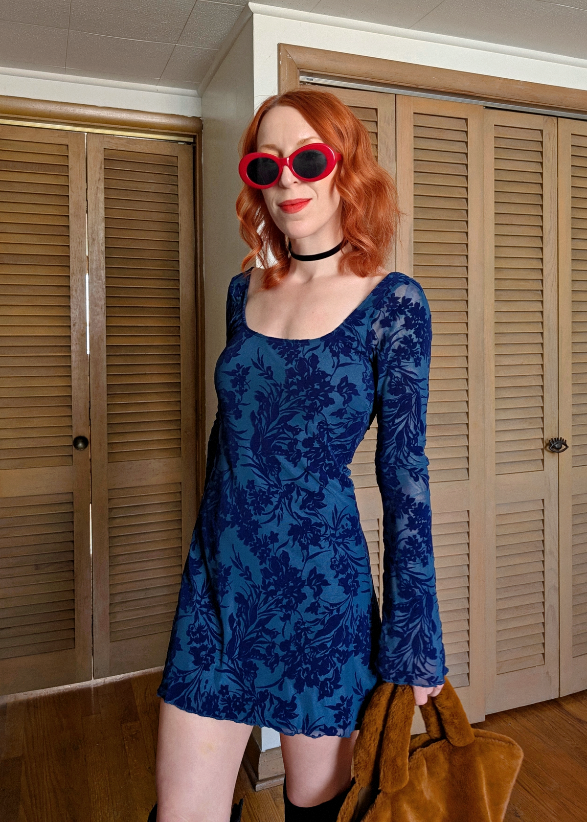 Woman wearing a blue floral dress and red sunglasses indoors.