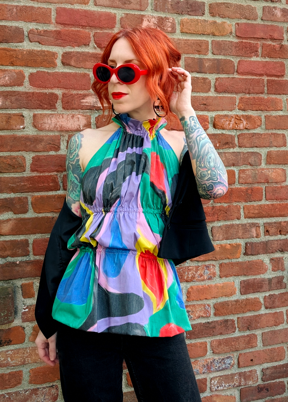 Person wearing a colorful halter top and black vest against a brick wall