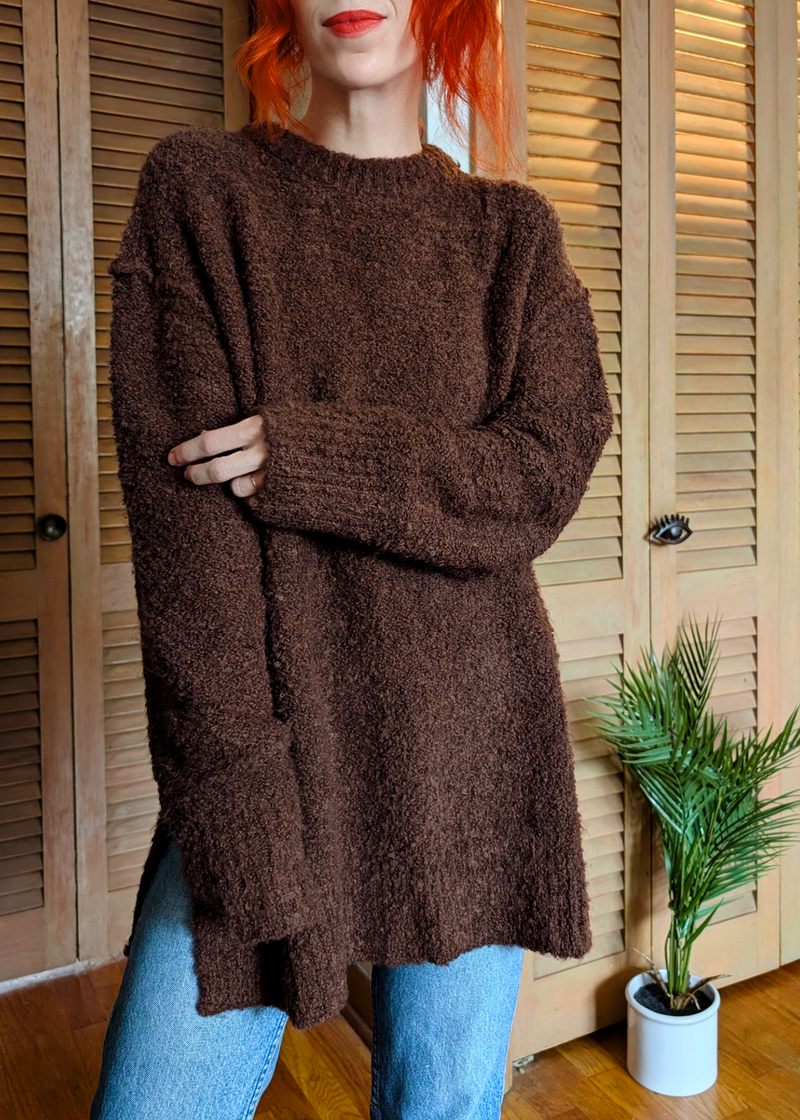 Person wearing a brown sweater in front of wooden shutters