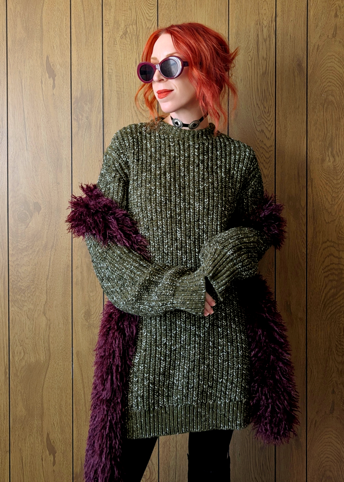 Person wearing a chunky green fleck tunic sweater styled with a purple scarf against a wooden background