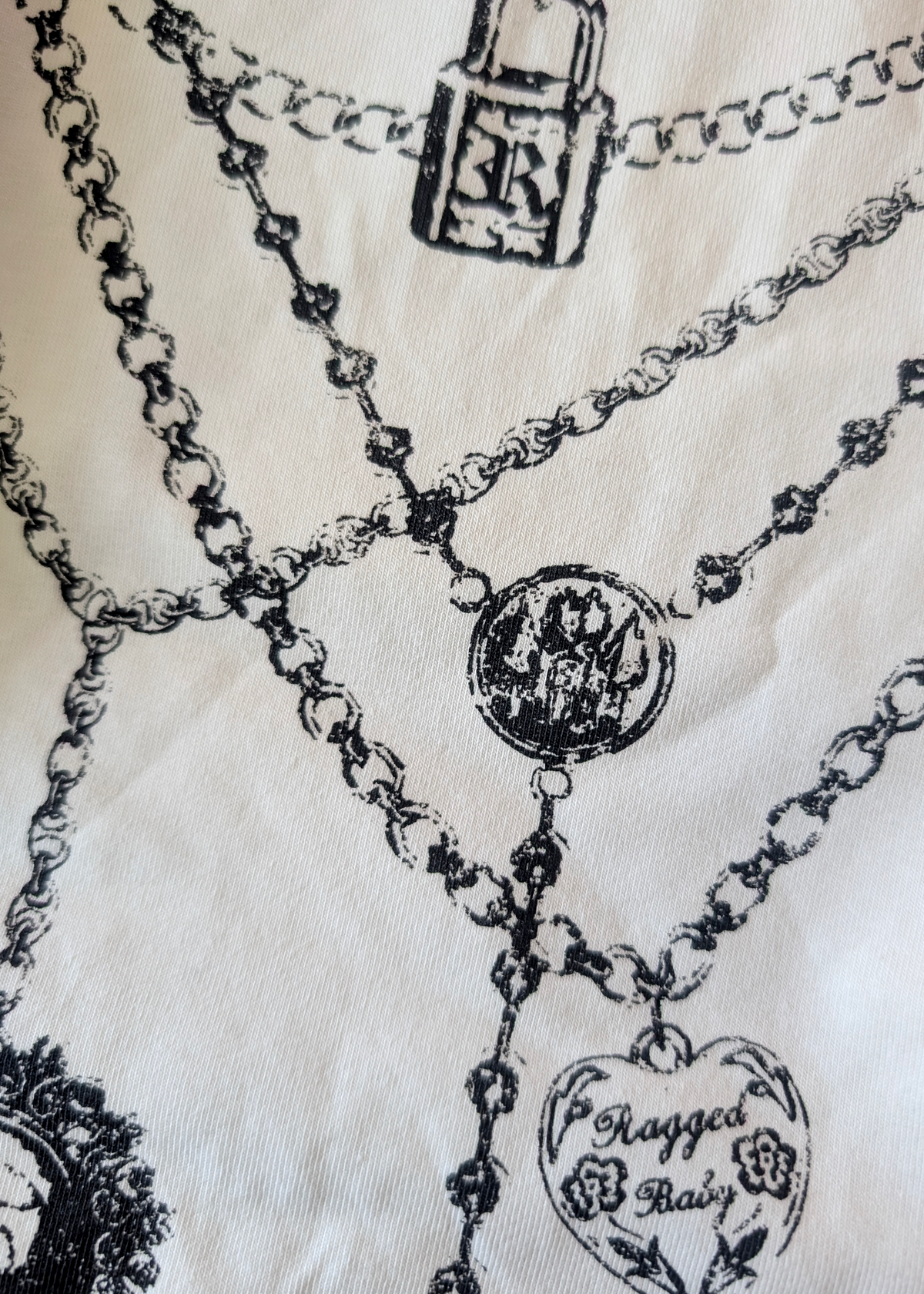 Close-up  detail of graphics of necklaces with various charms on an ivory tee
