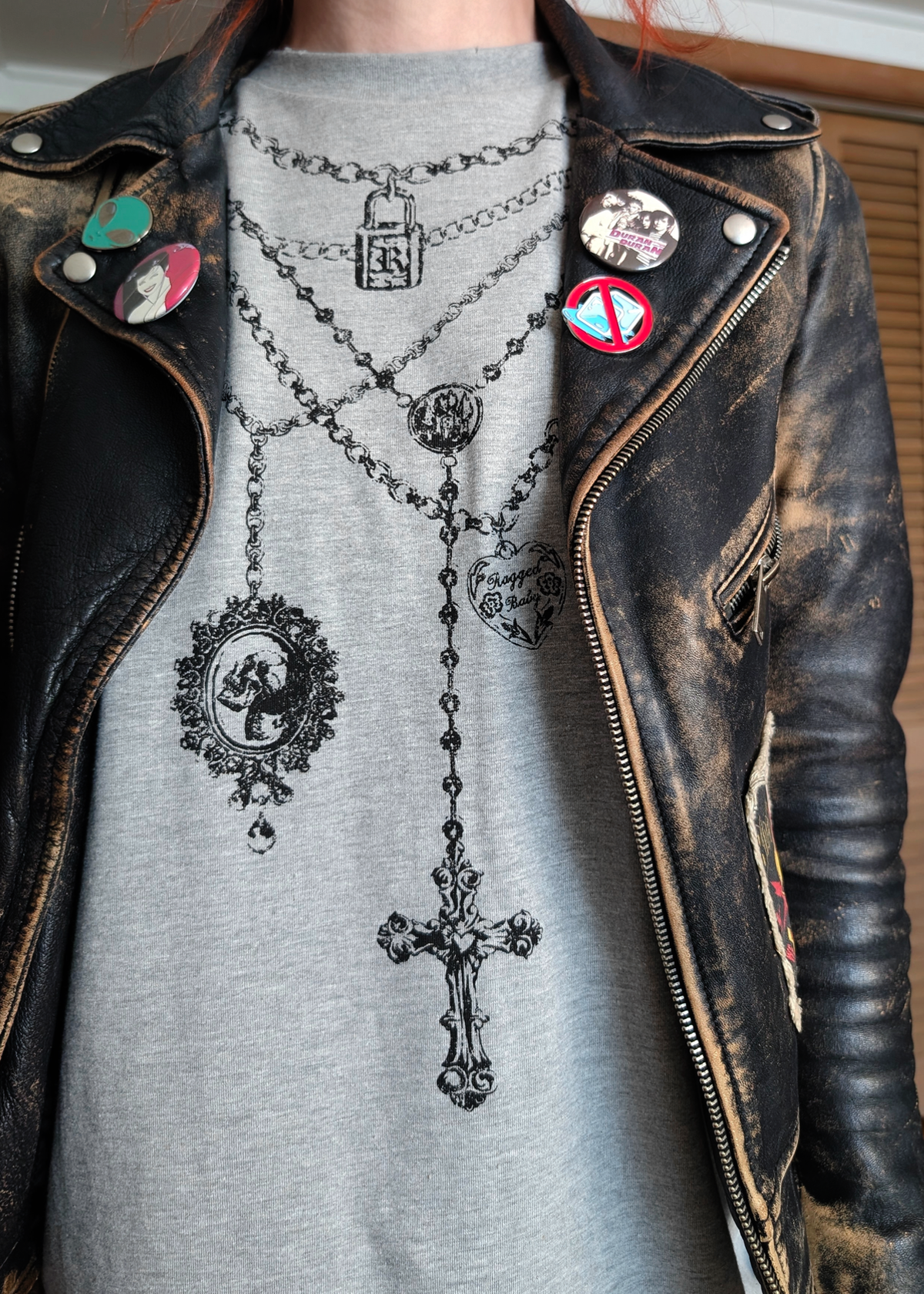 Person wearing a black leather jacket and an oversized gray shirt with necklace graphics at front