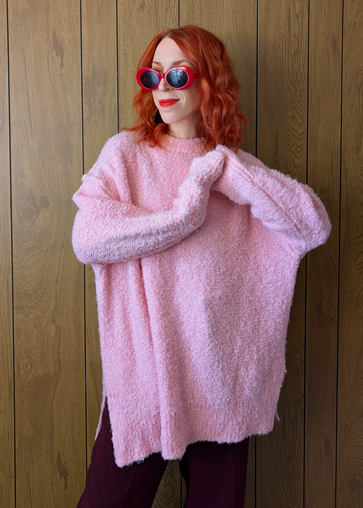 Person wearing a pink fluffy sweater and sunglasses against a wooden background