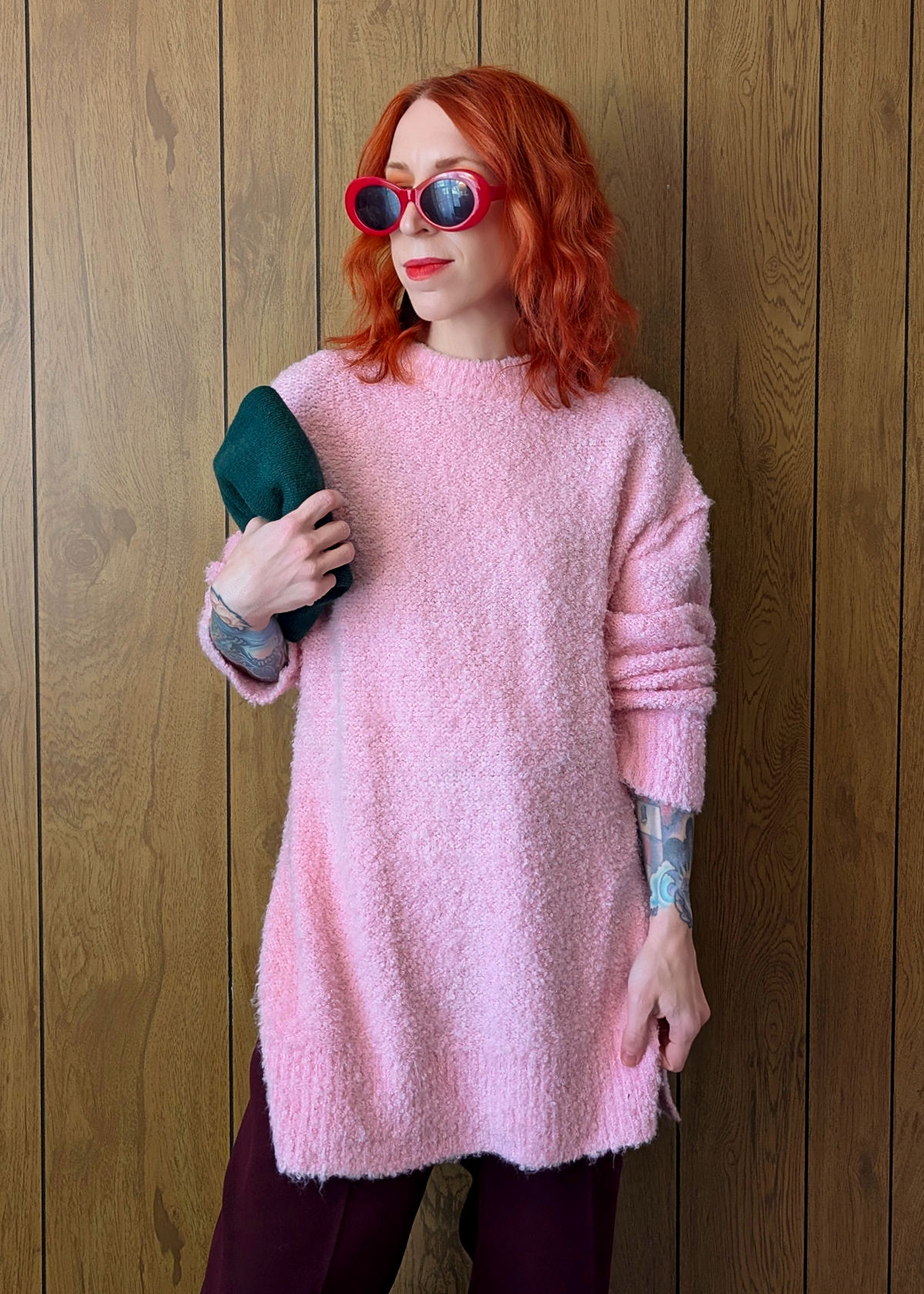 Person wearing a pink sweater and sunglasses against a wooden wall
