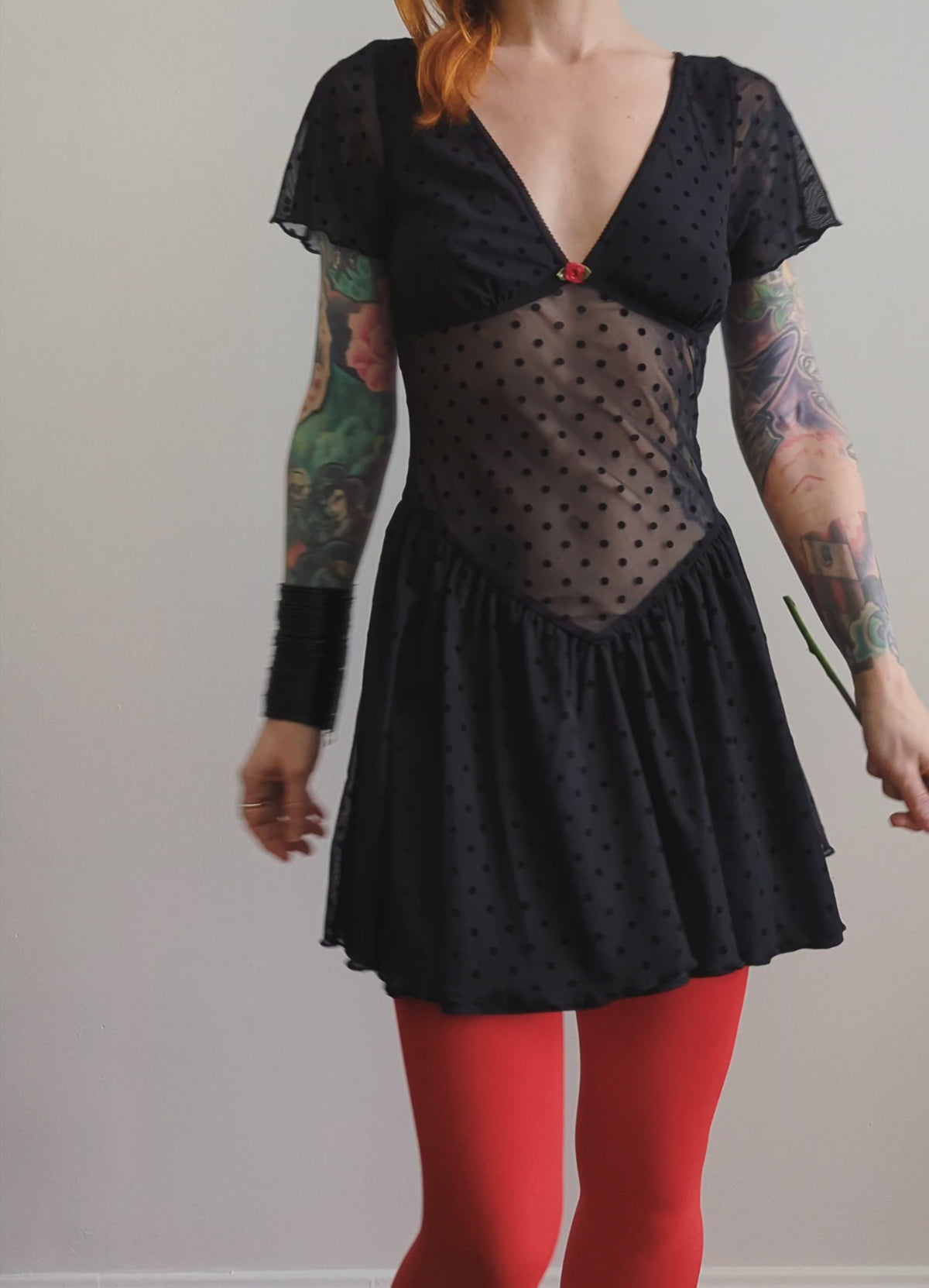 90s inspired black mesh mini dress with black velvet flocked dots allover. Features flutter short sleeves, v-neckline with red satin rosette, sheer waist, and floaty skirt. By Motel Rocks