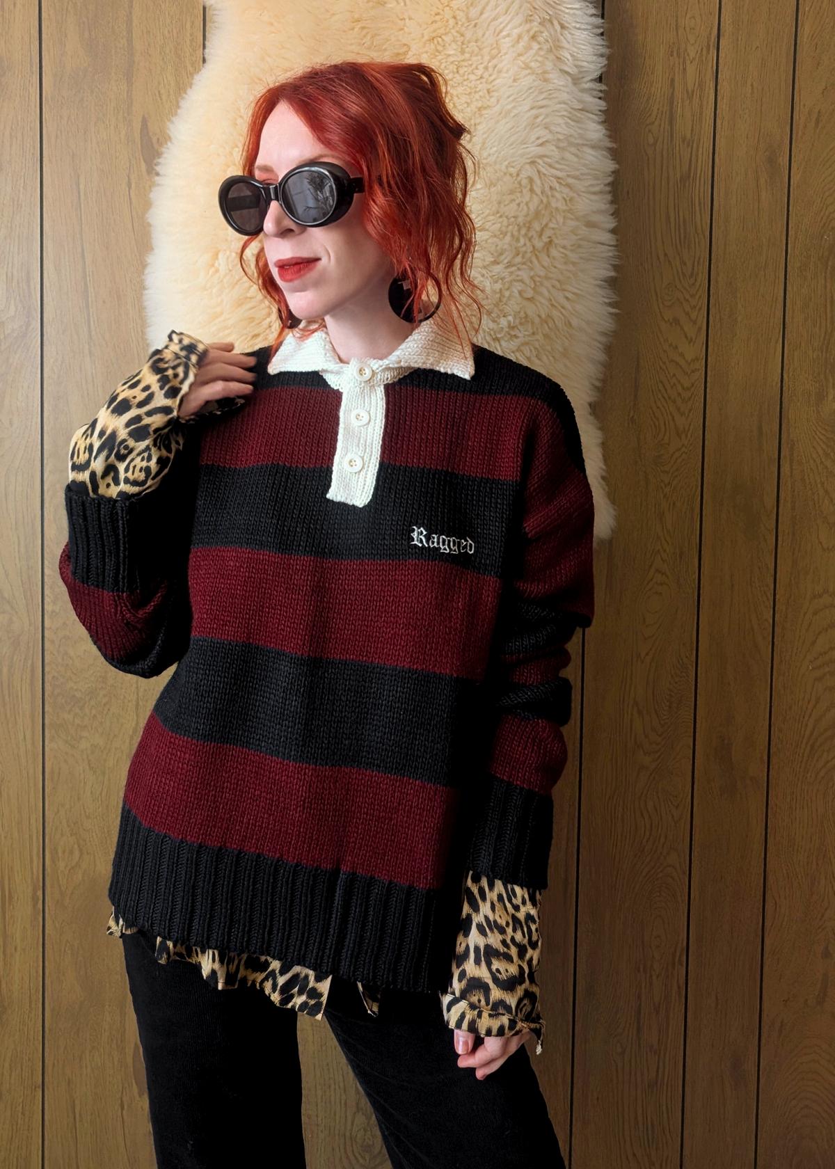 Person wearing a black and red striped polo sweater over a leopard print shirt, standing against a wooden wall.