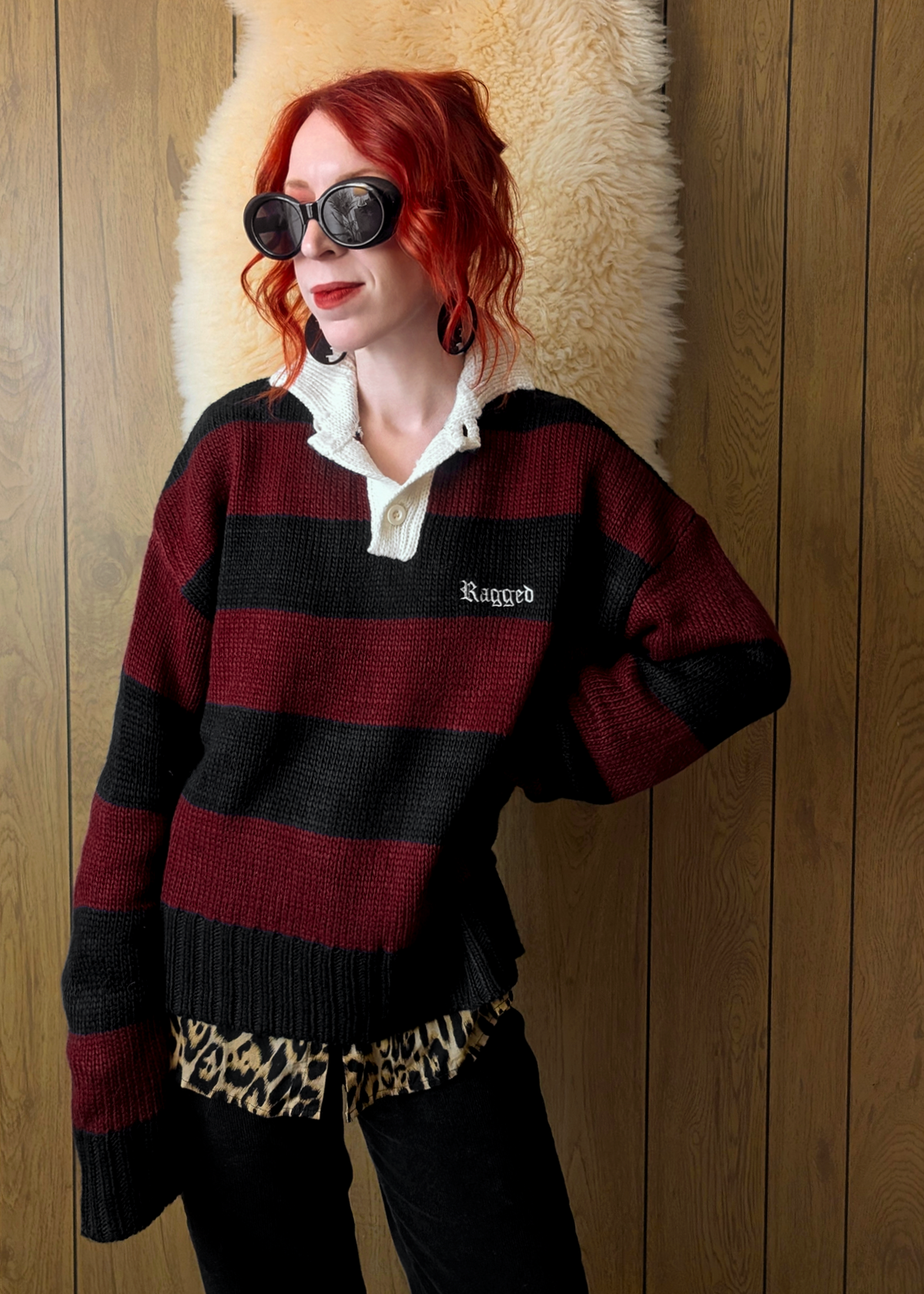 Person wearing a striped sweater with a leopard print shirt underneath, lagainst a wooden wall.