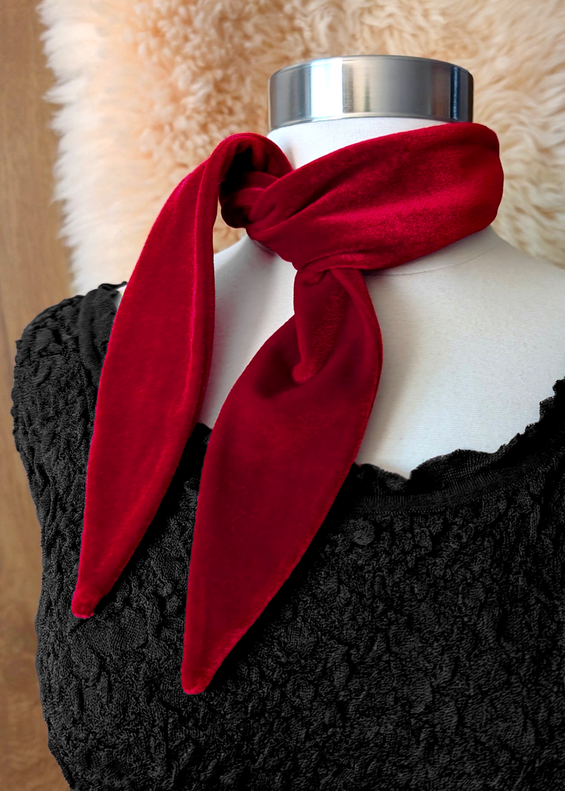 Mannequin wearing a red velvet scarf. Wooden backdrop with faux fur drape.