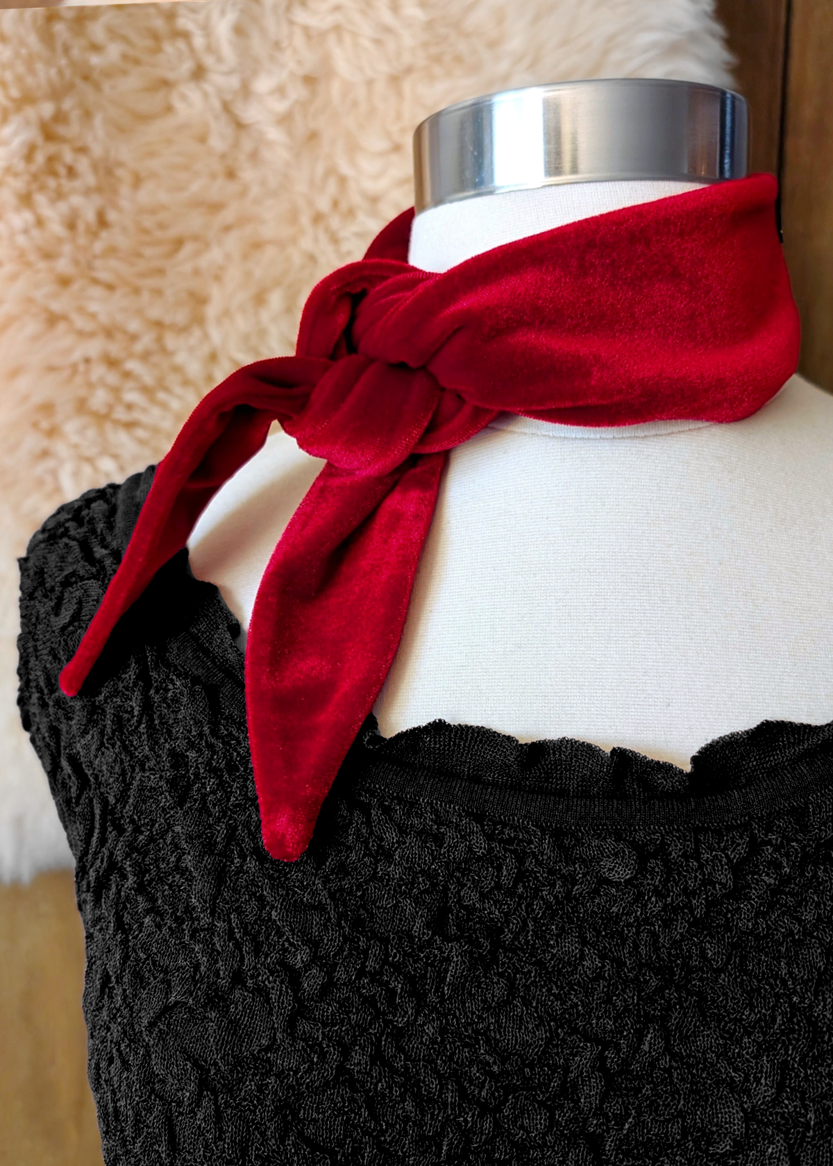 Mannequin wearing a red velvet scarf. Wooden backdrop with faux fur drape.