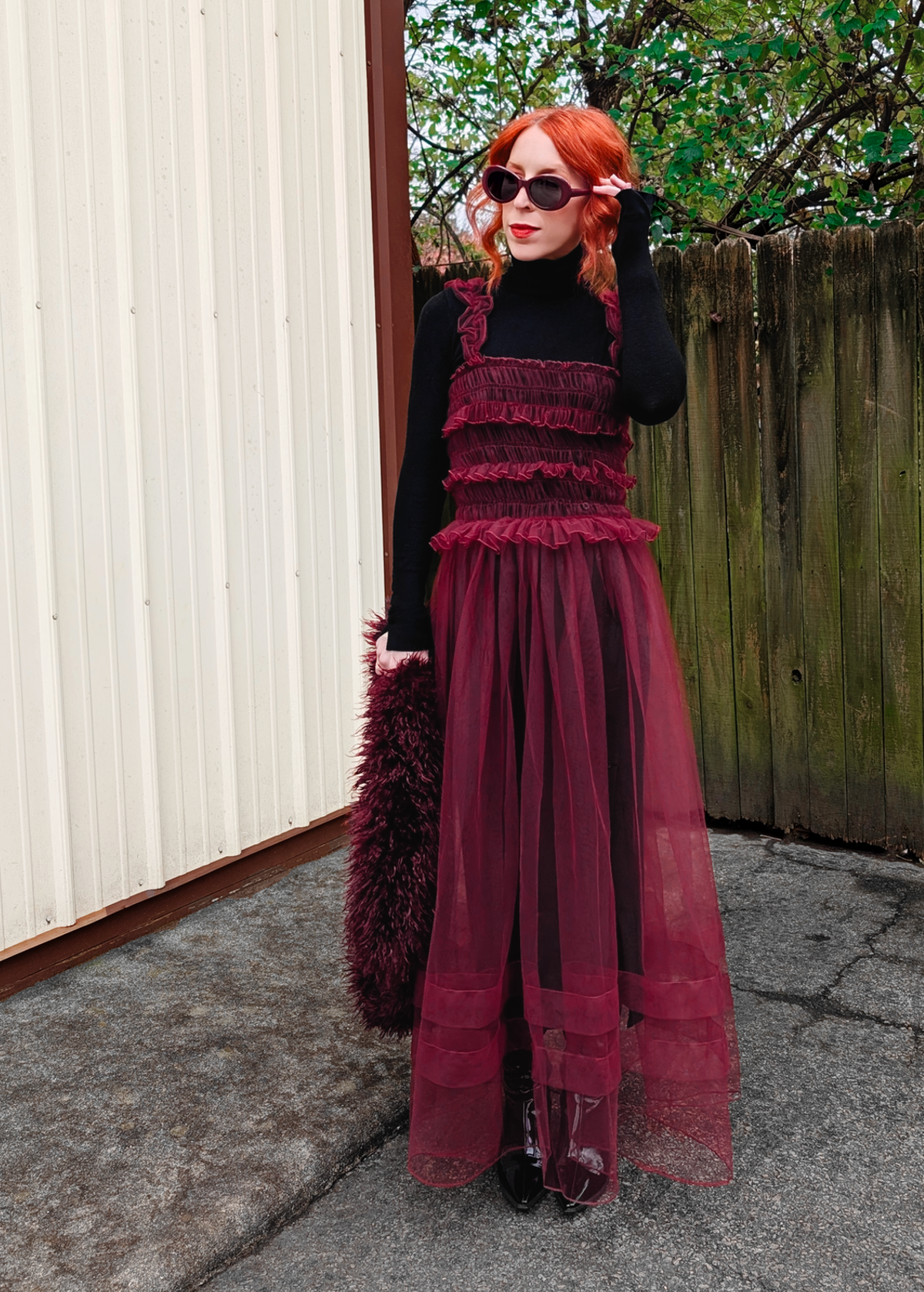 Person wearing a black top and burgundy sheer tulle dress standing outdoors.