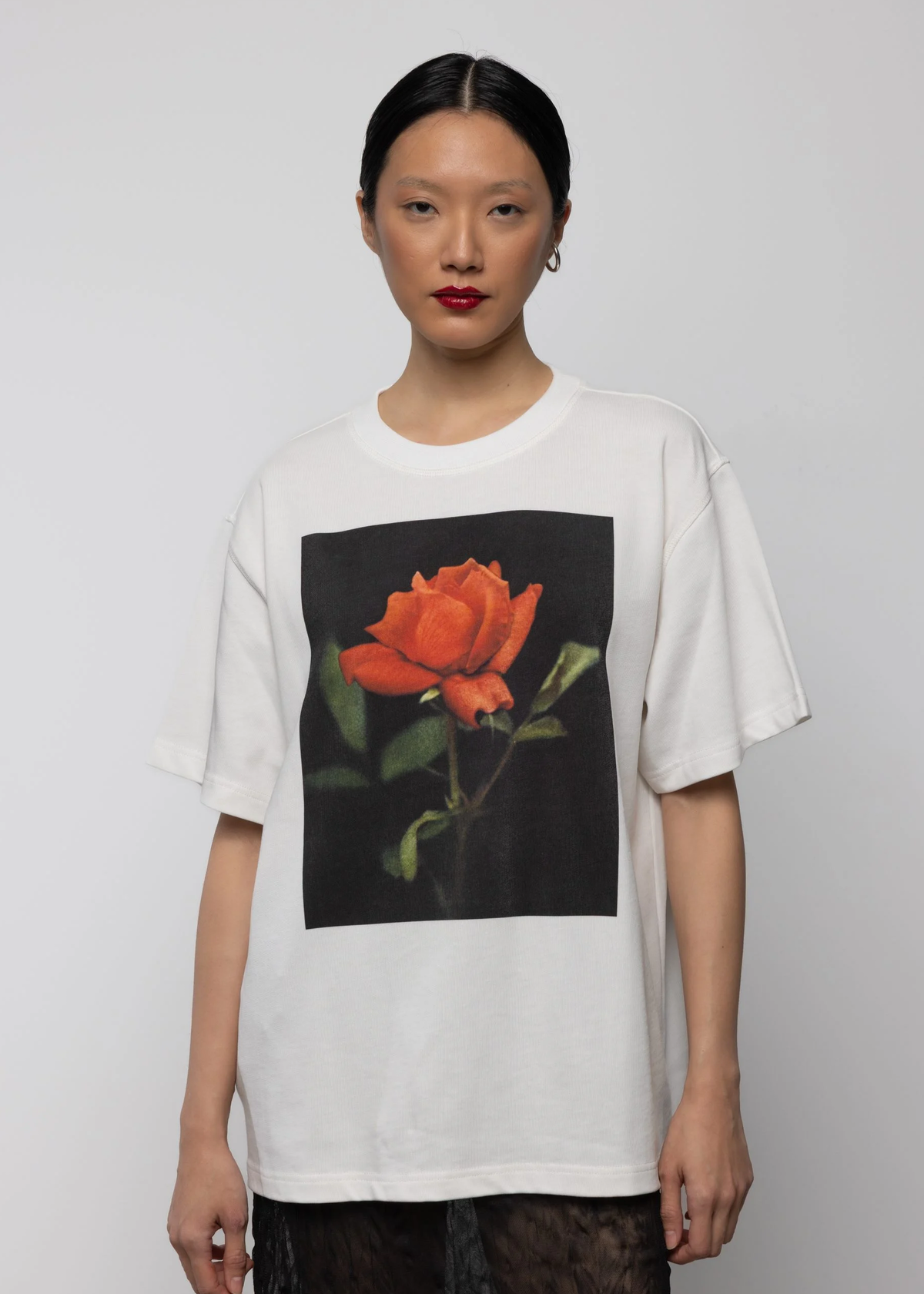Person wearing a white t-shirt with a red rose graphic on a plain background
