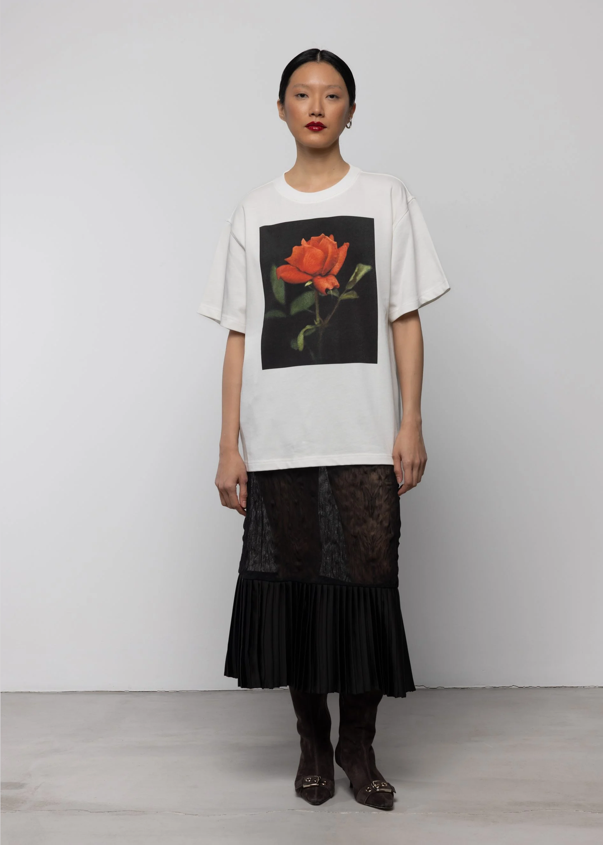 Woman wearing a white t-shirt with a floral design and a black lace skirt on a plain background