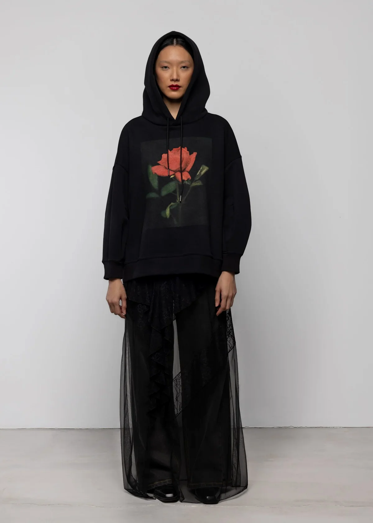 Person wearing a black hoodie with a floral design on a plain background