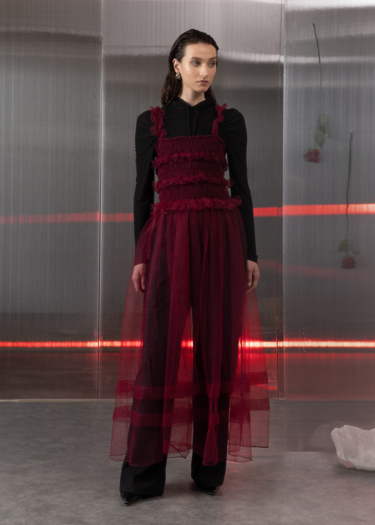 Model wearing a burgundy tulle dress with ruffled details against a reflective surface.