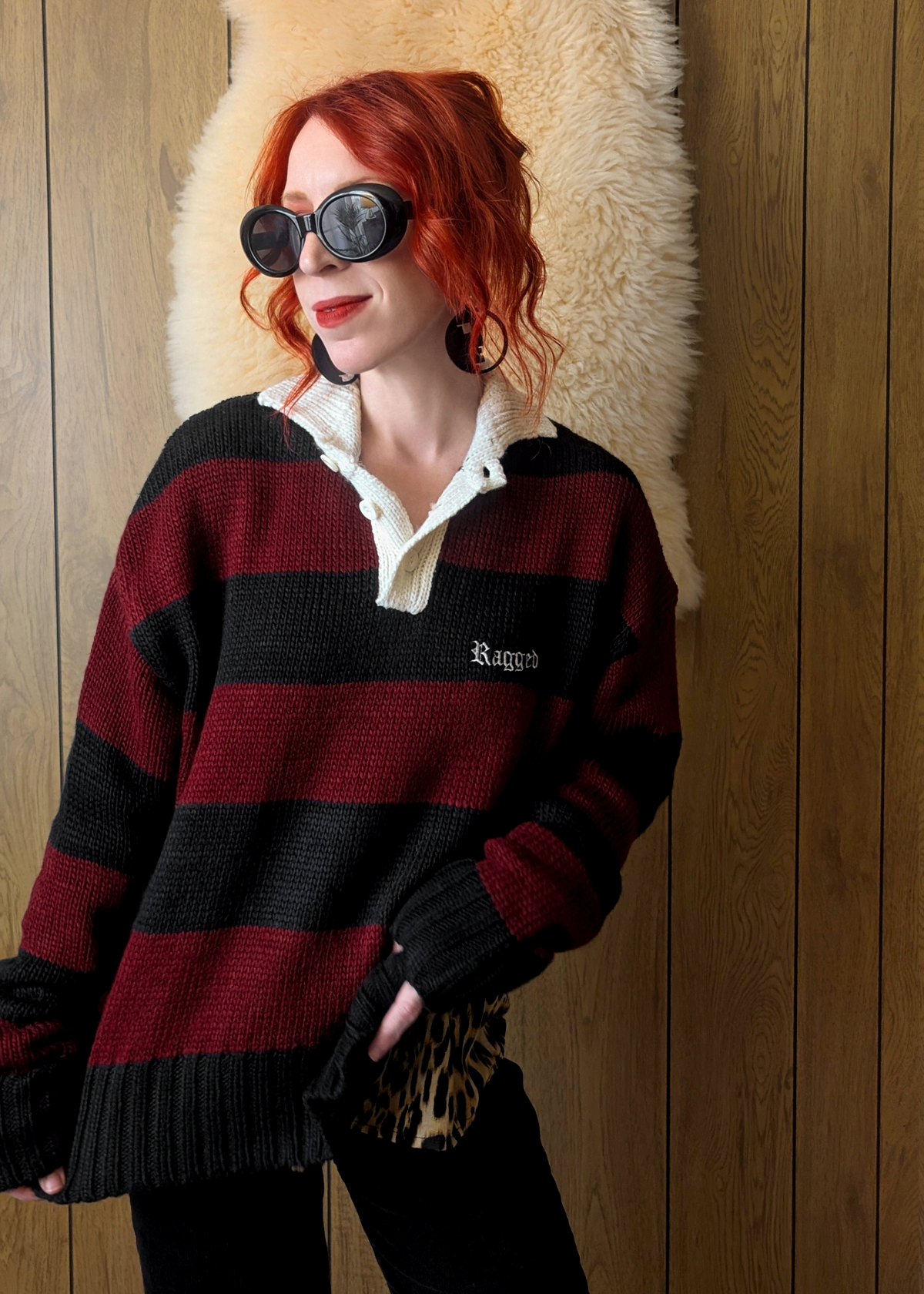 Person wearing a red and black striped sweater with 'Ragged' logo, standing against a wooden wall.