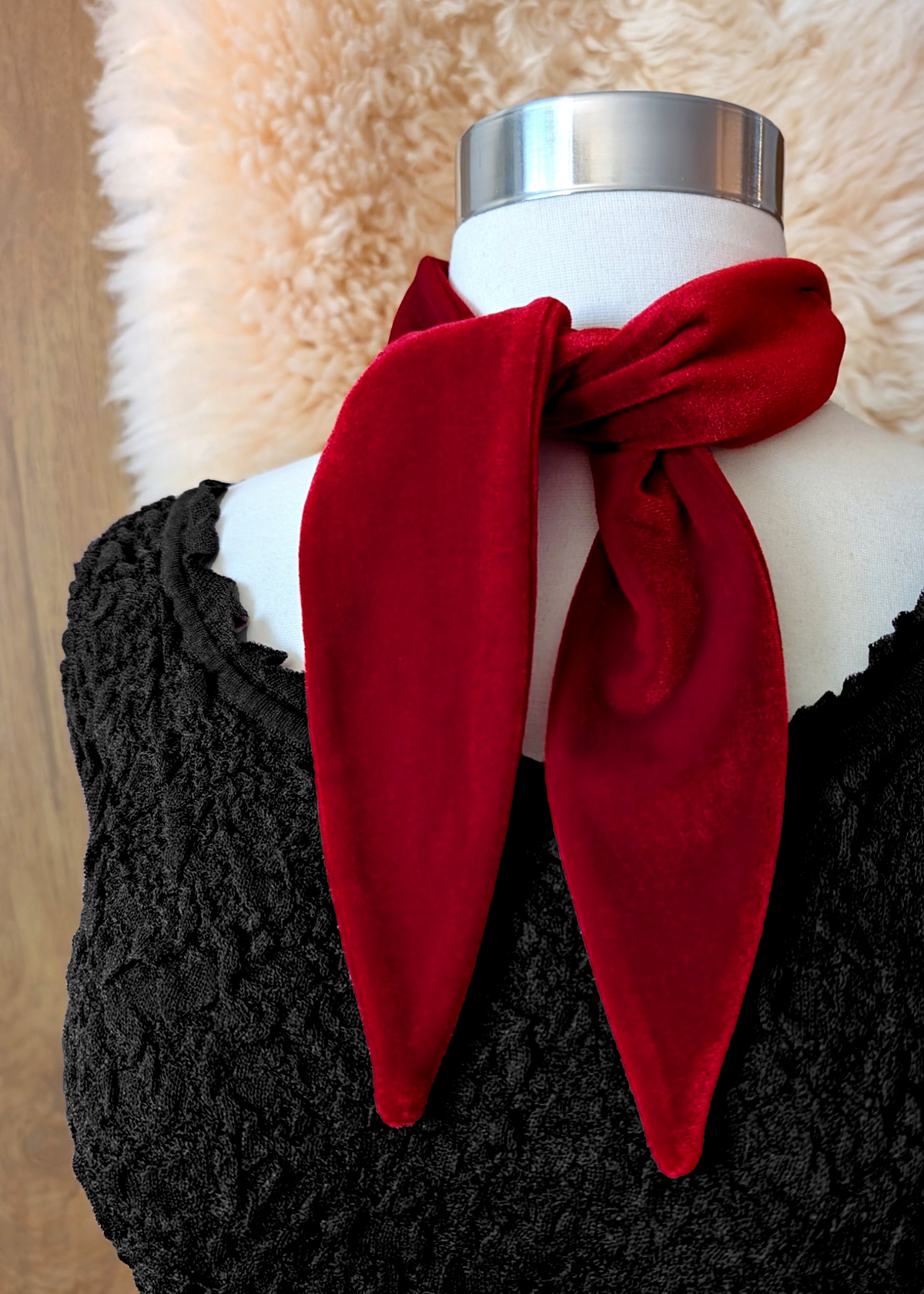 Mannequin wearing a red velvet scarf. Wooden backdrop with faux fur drape.