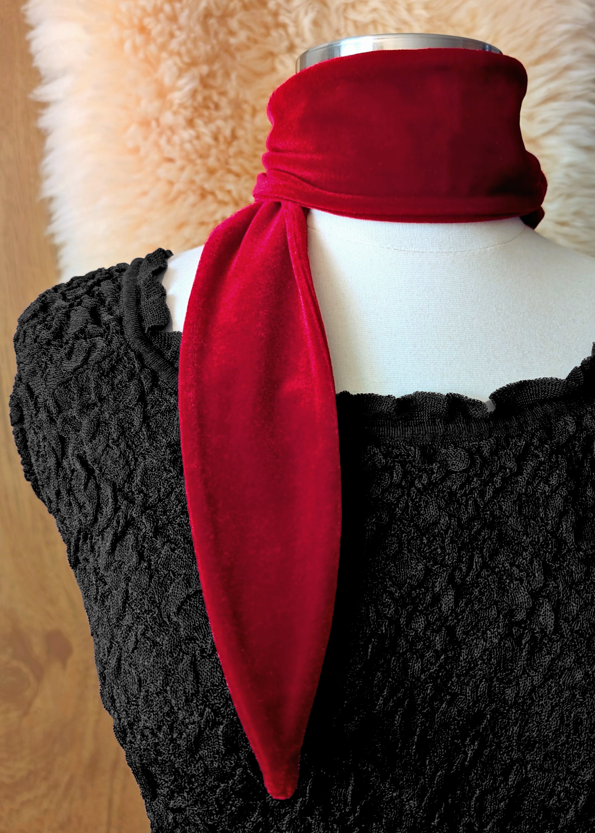 Mannequin wearing a red velvet scarf wrapped around the neck. Wooden backdrop with faux fur drape.
