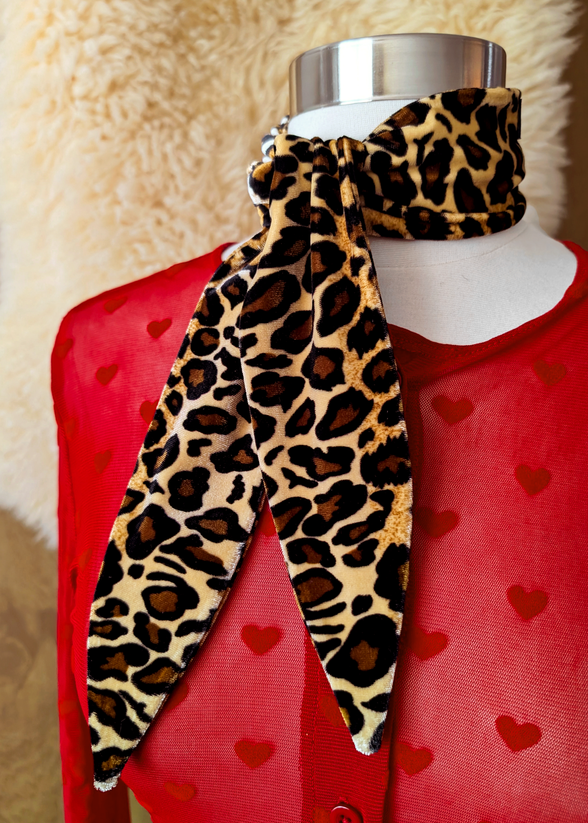 Mannequin wearing a red cardigan with heart patterns and a leopard print vevet scarf.