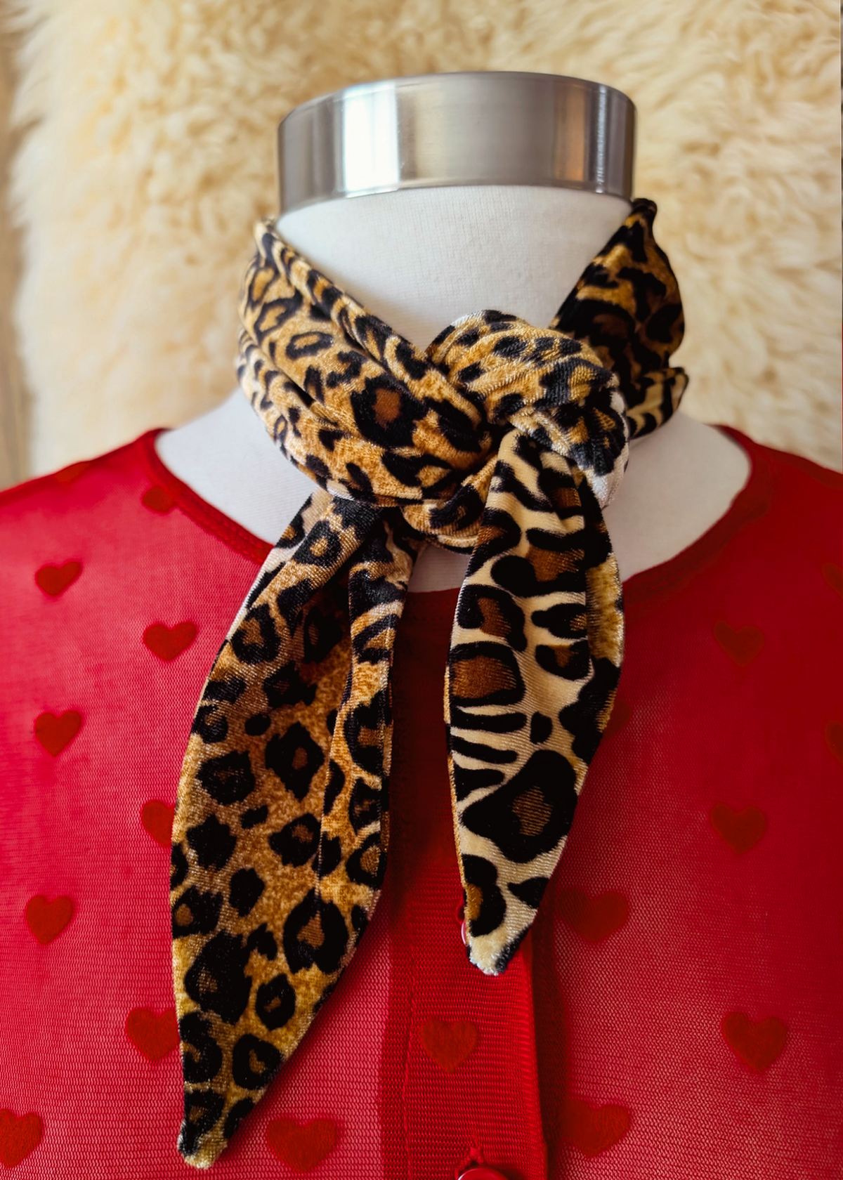Mannequin wearing a red cardigan with heart patterns and a leopard print vevet scarf.