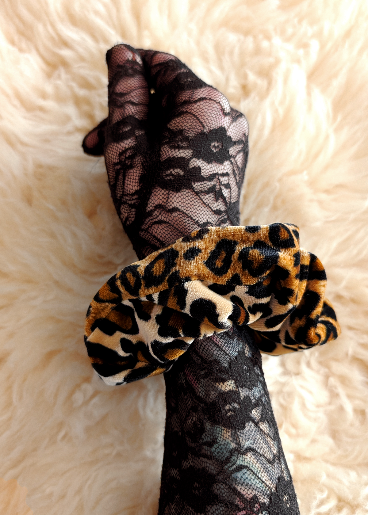Black lace gloves with a leopard print scrunchie on a beige textured background