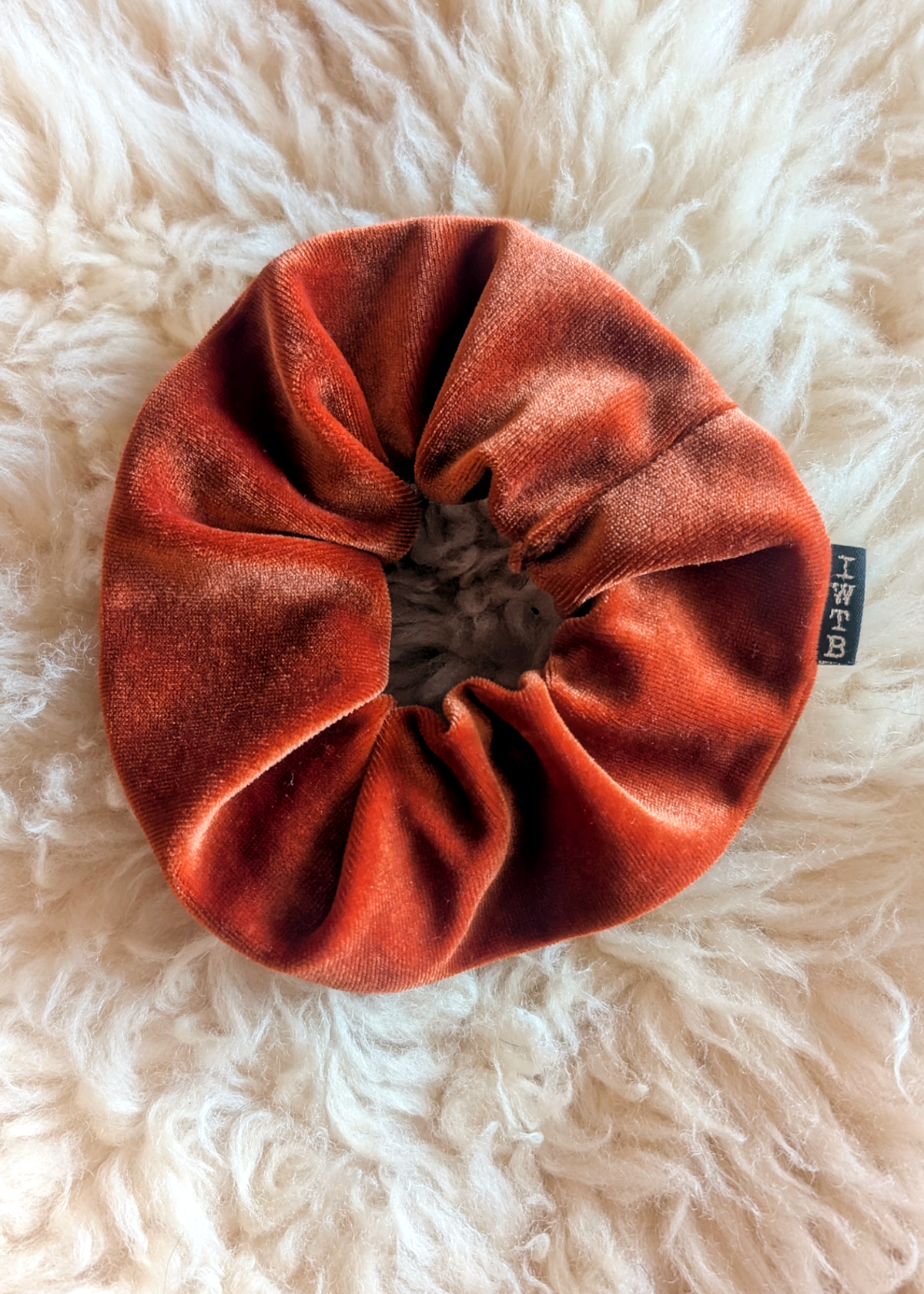 Orange velvet scrunchie on a fluffy white surface