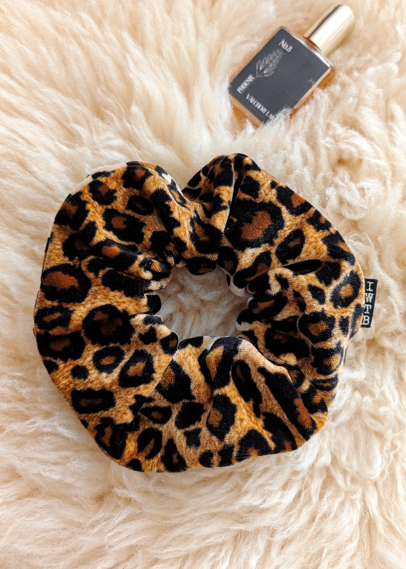 Leopard print scrunchie on a fluffy white surface with a perfume bottle in the background.