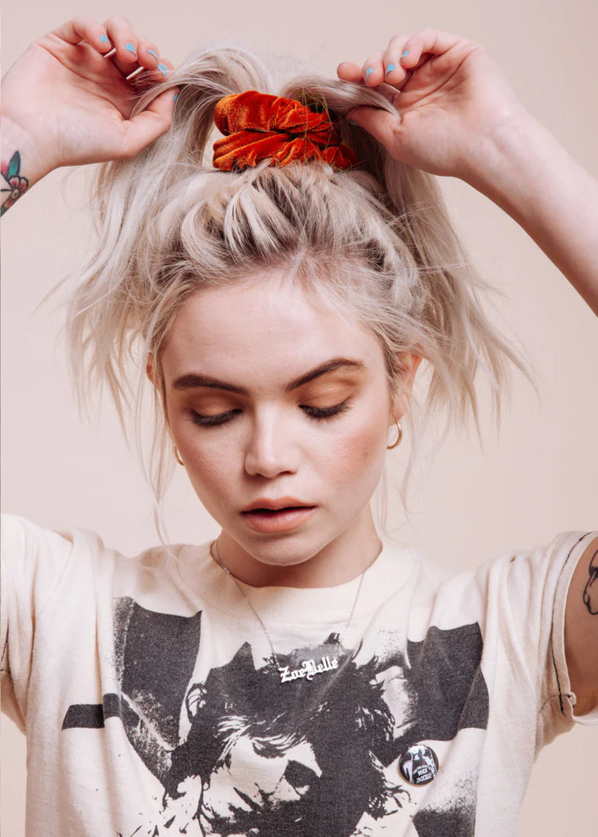 Person with styled hair wearing a burnt orange velvet scrunchie and a graphic t-shirt against a neutral background
