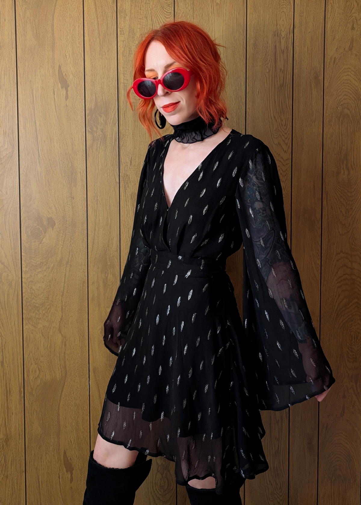 Person wearing a black dress with sheer bell flare sleeves against a wooden background