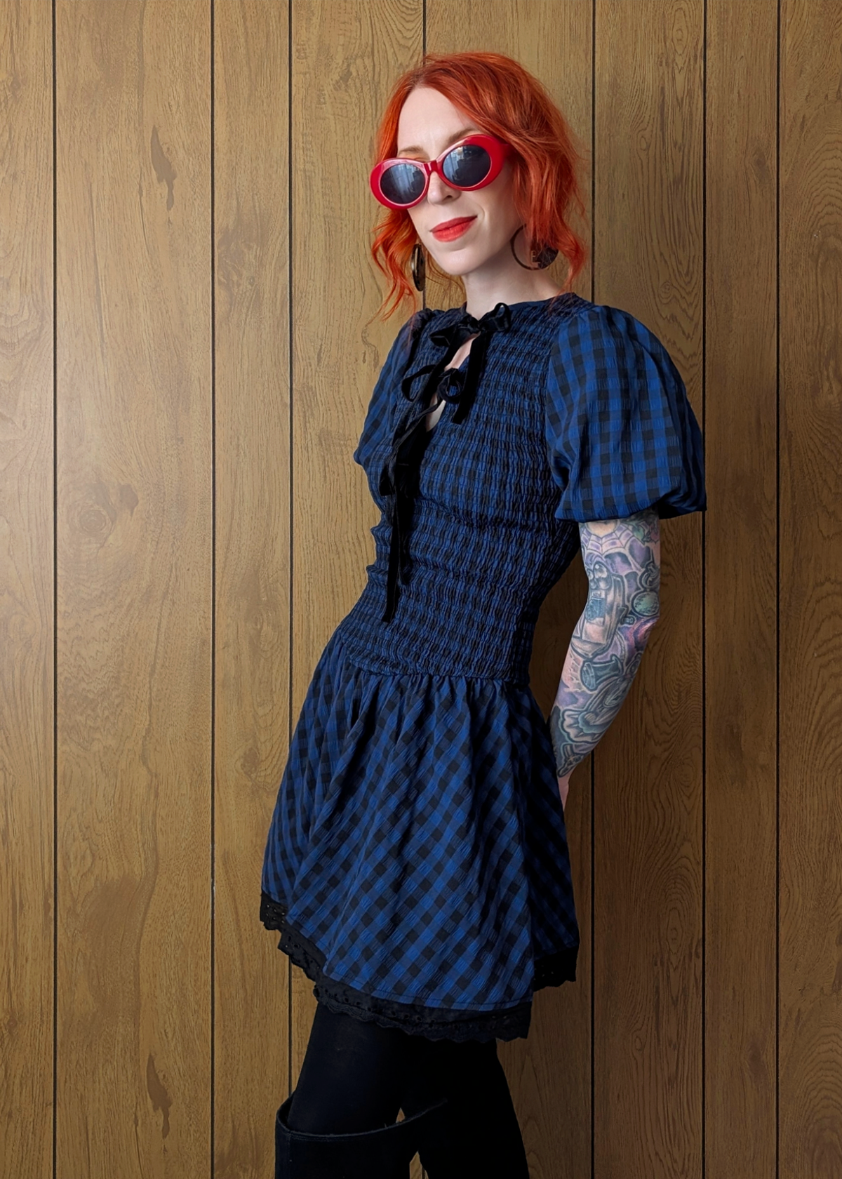 Person wearing a blue checkered dress and sunglasses against a wooden panel background