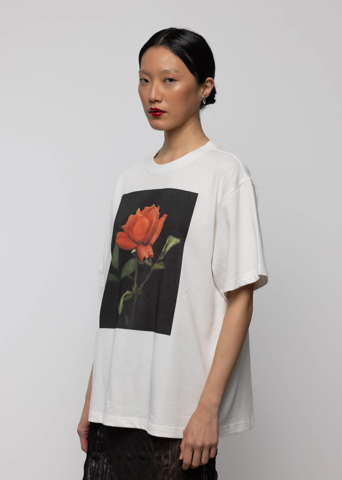 Woman wearing a white t-shirt with a red rose graphic on a plain background