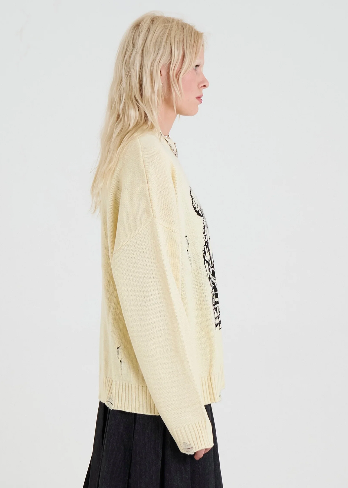 Side view of a blonde woman wearing an oversized cream sweater 