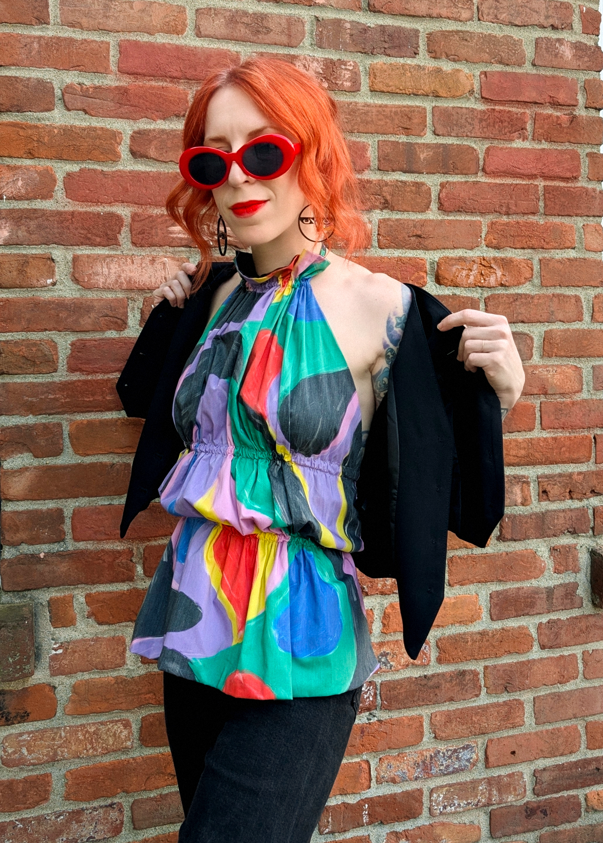 Person wearing a colorful halter top and black vest against a brick wall