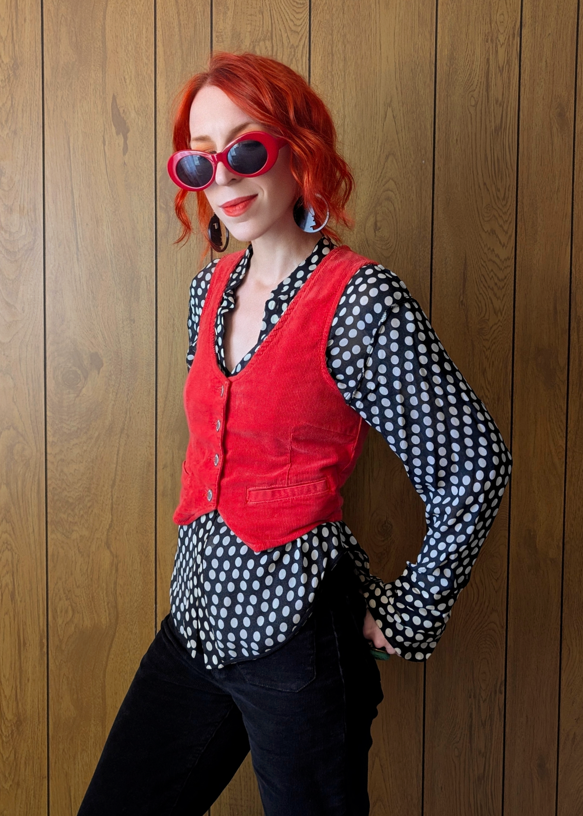 Person wearing a red vest over a polka dot shirt against a wooden background