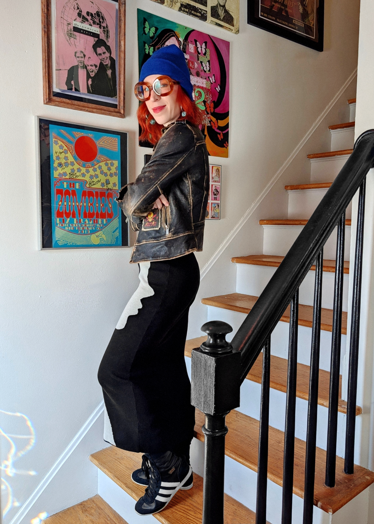 Person standing on a staircase wearing a black knit dress with colorful artwork on the walls