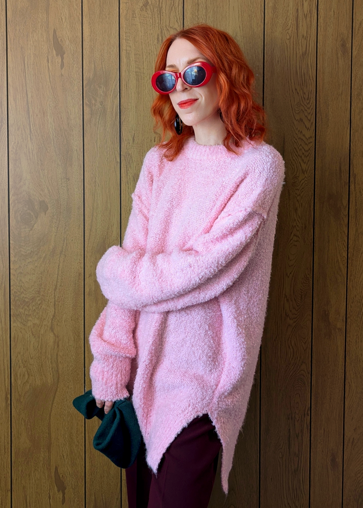 Person wearing a pink fluffy sweater and red sunglasses against a wooden background