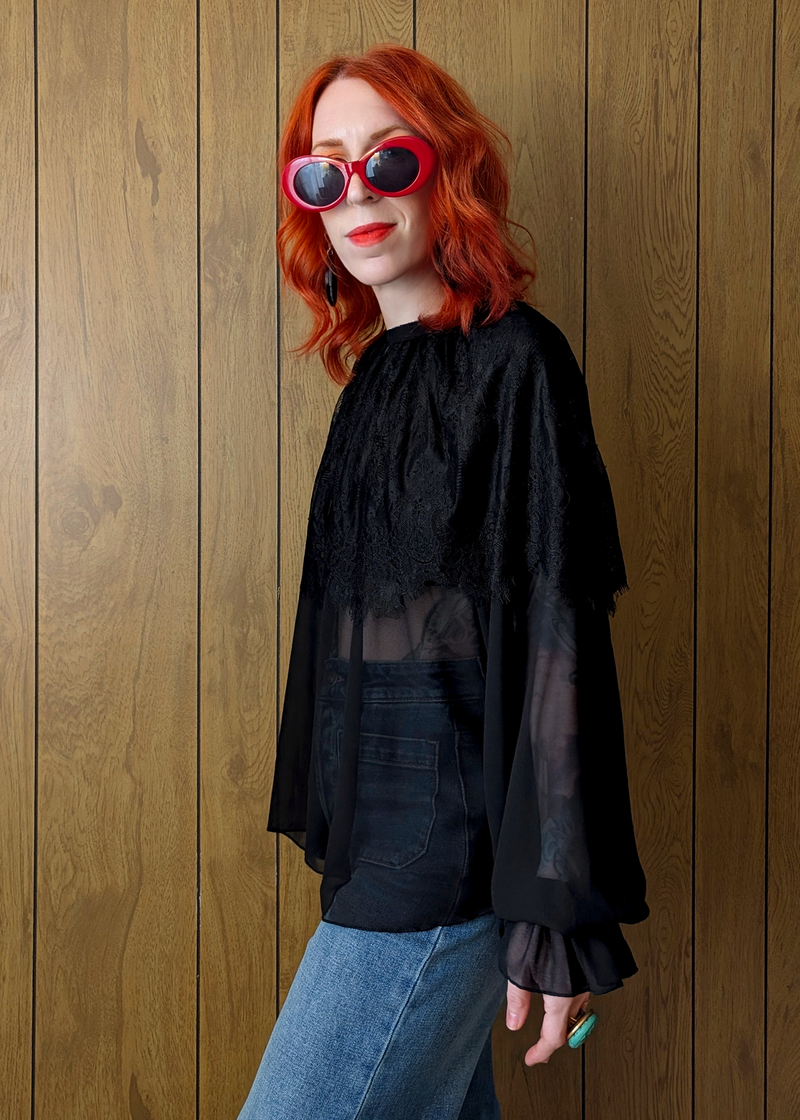 Person wearing a black sheer top and blue jeans against a wooden panel background