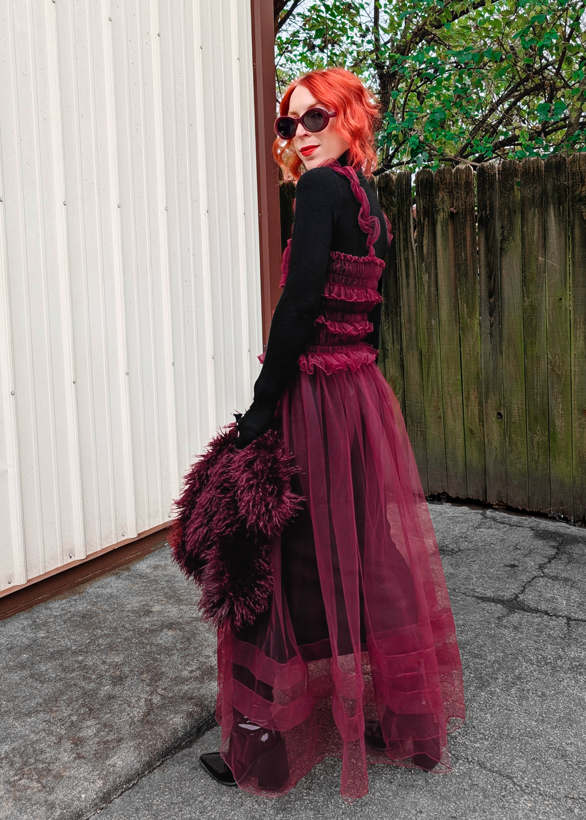 Person with red hair wearing a black turtleneck under a sheer burgundy tulle dress outdoors