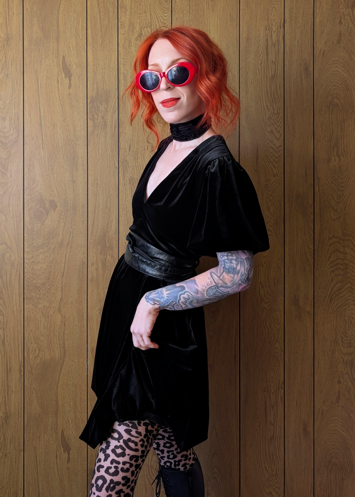 Person wearing a black velvet mini dress with leopard print leggings against a wooden background