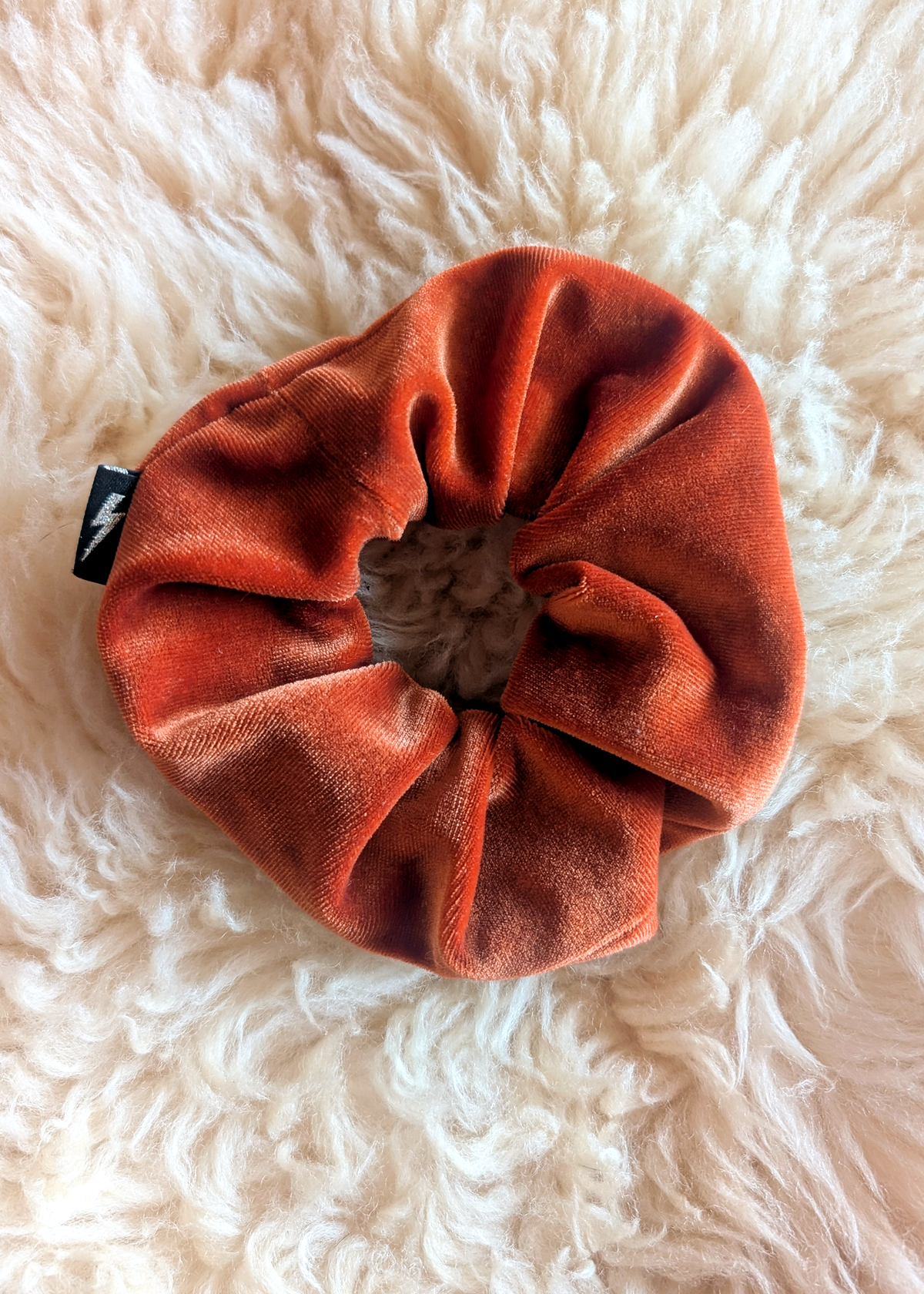Orange scrunchie with a brand tag on a fluffy white surface