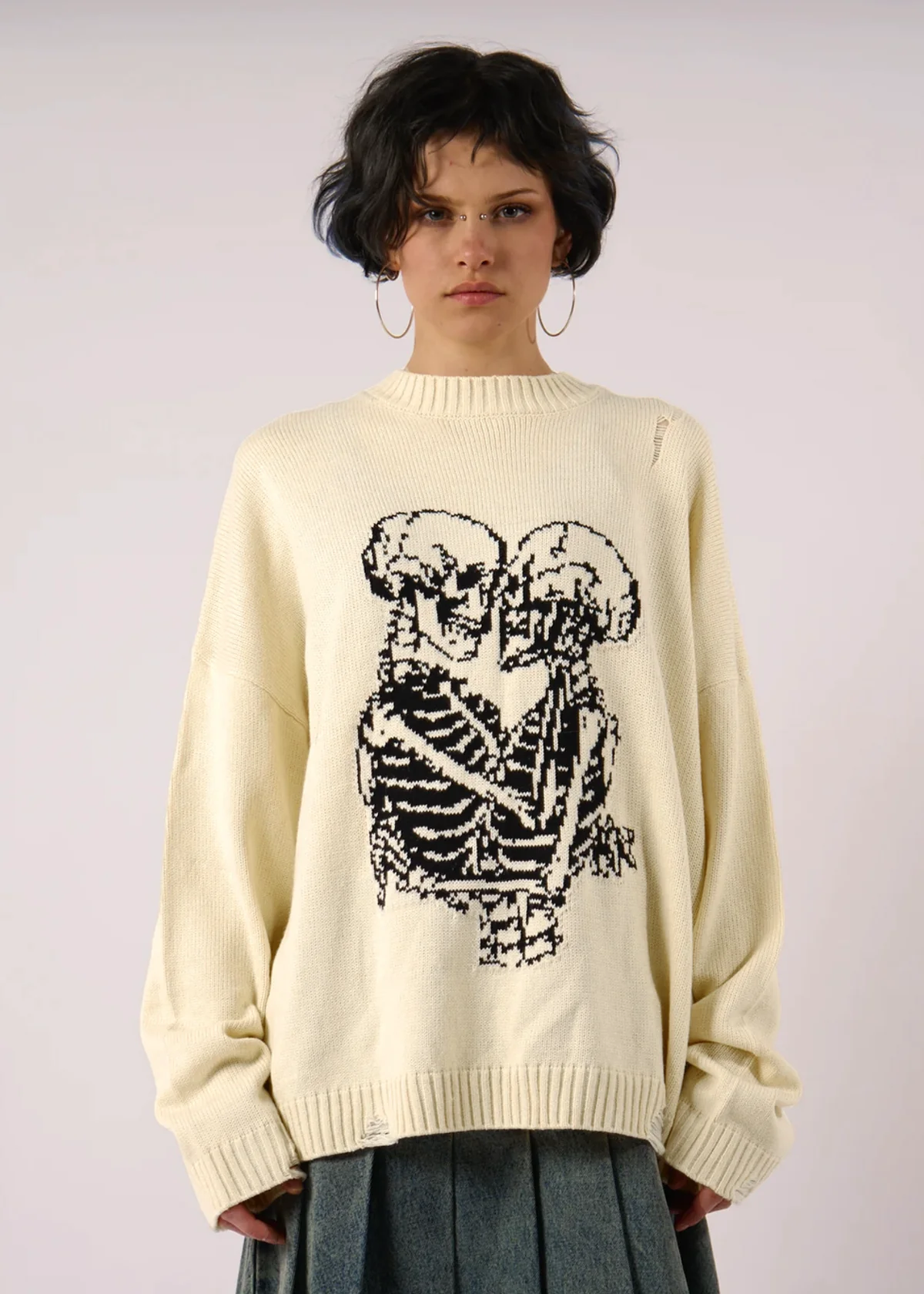 Person wearing a cream sweater with a black skeleton design on a plain background