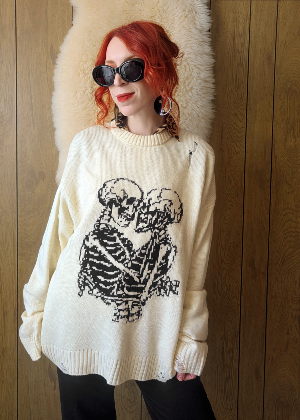 Person wearing a cream sweater with a black skeleton design against a wooden wall.