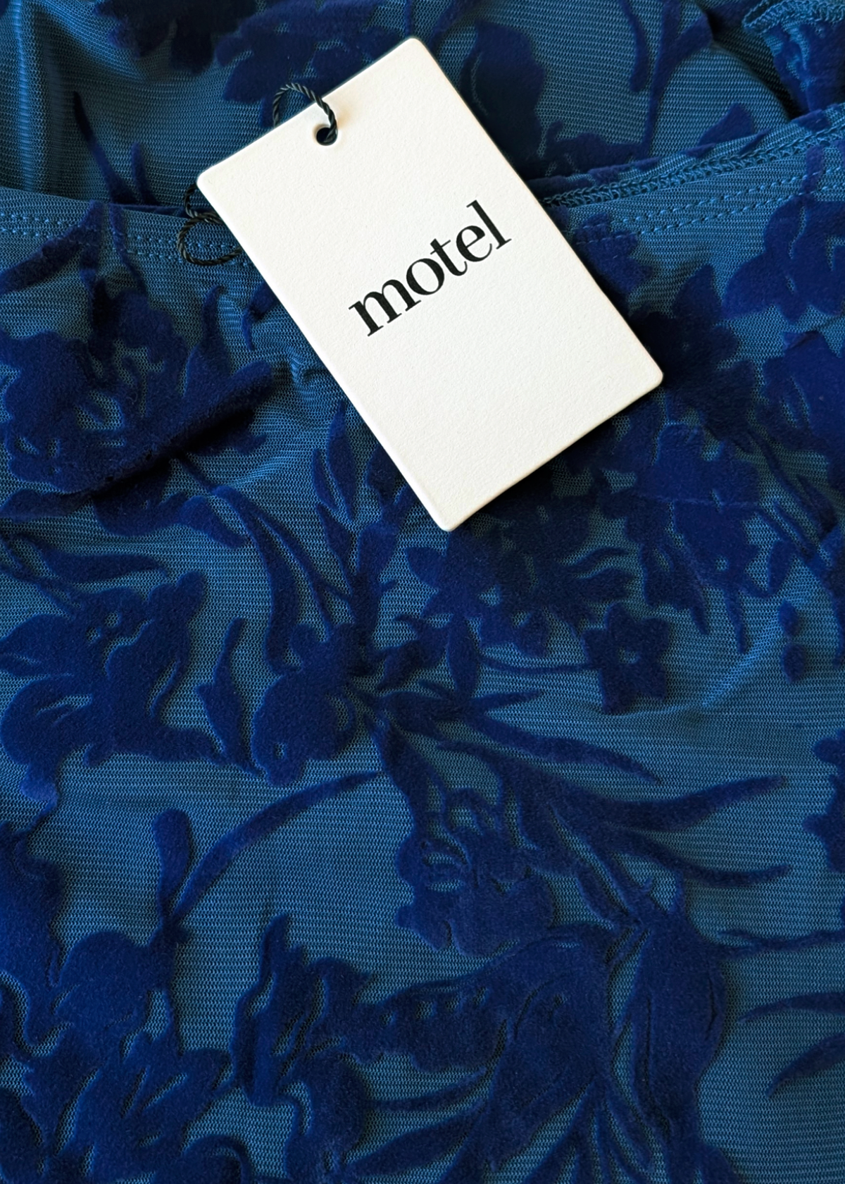 Blue flocked mesh floral fabric with a 'motel' tag
