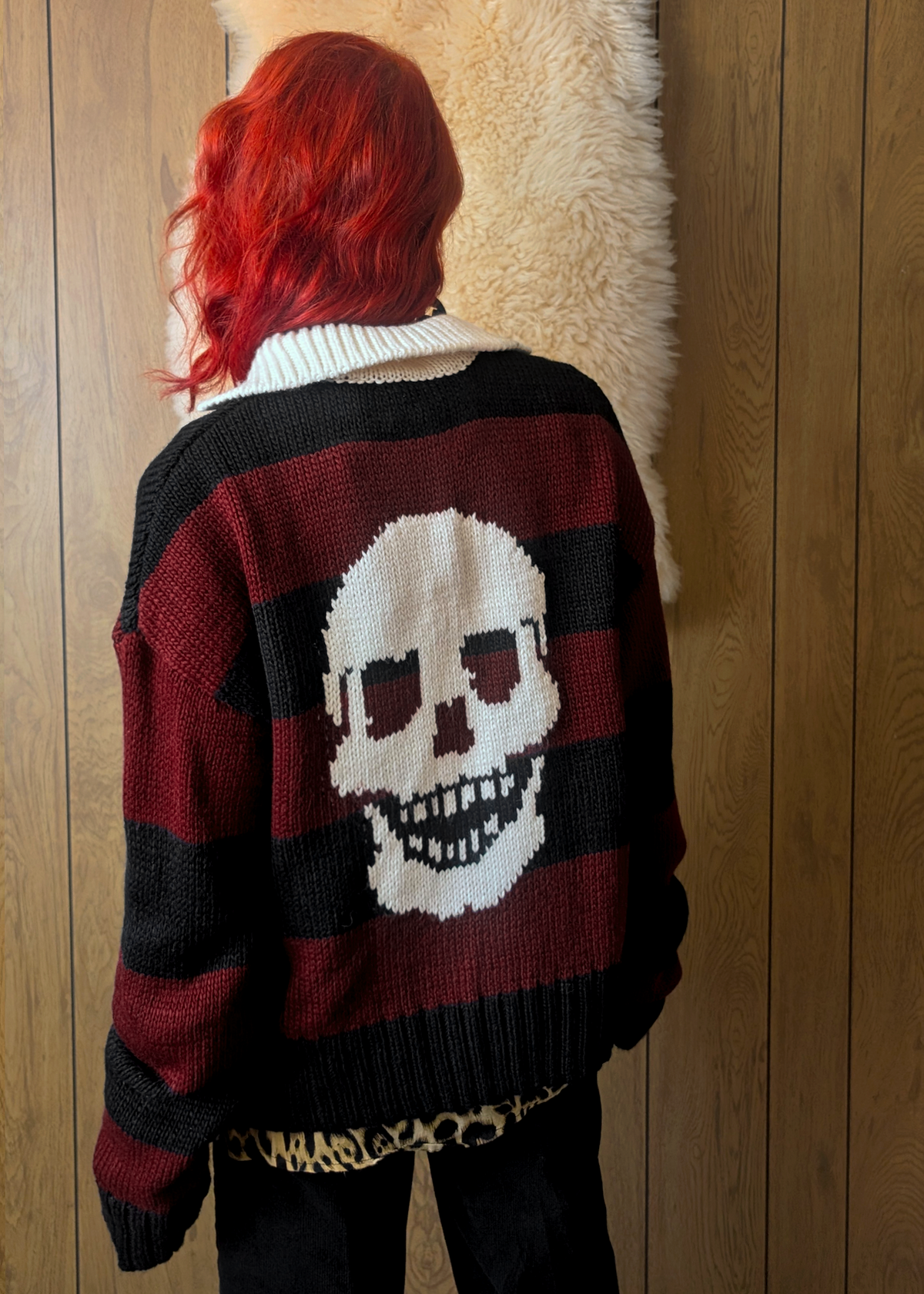 Person wearing a striped sweater with a skull design in front of a wooden wall.