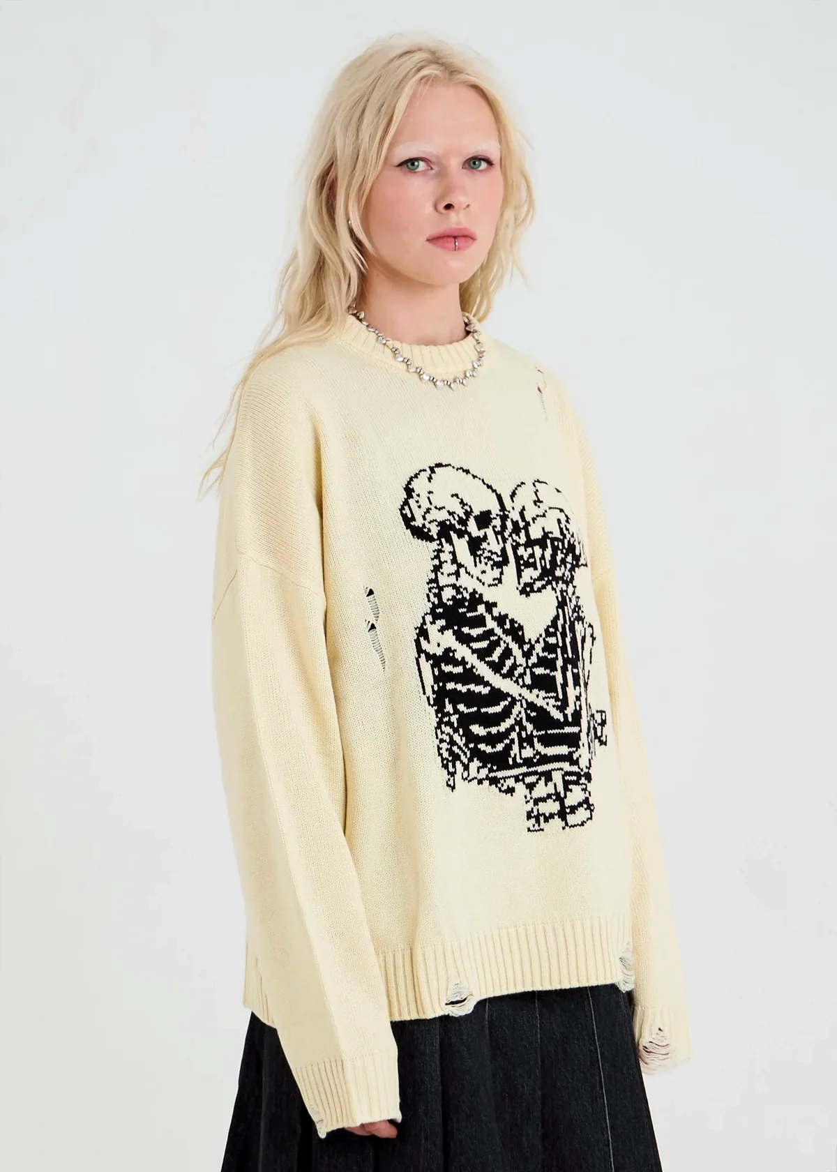 Person wearing a cream sweater with a black skeleton design on a white background
